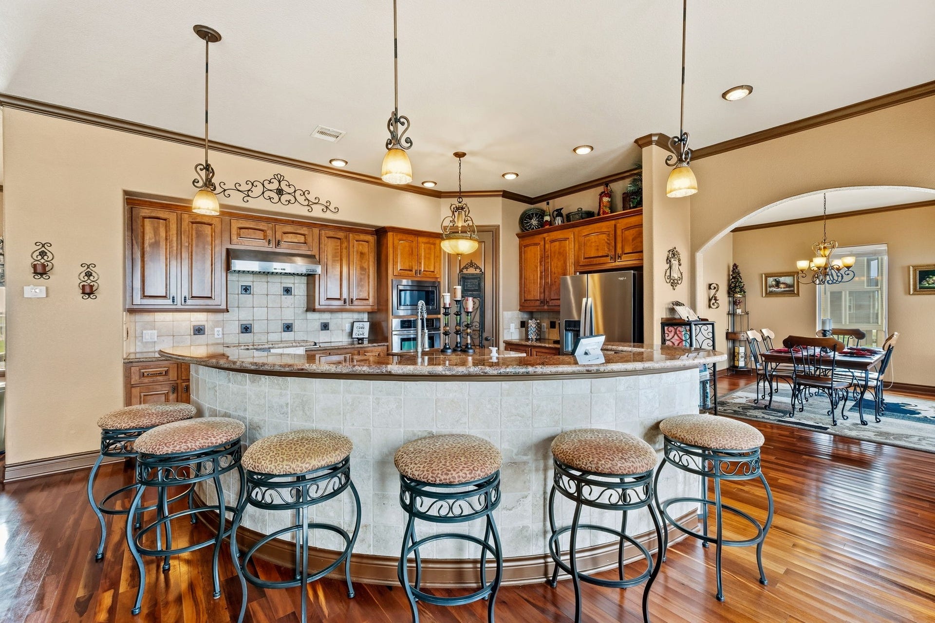 26 Half Moon, Hitchcock, TX 77563 Spacious kitchen with rich wood cabinetry, a large curved island with seating, and elegant pendant lighting, seamlessly connecting to a cozy dining area.
