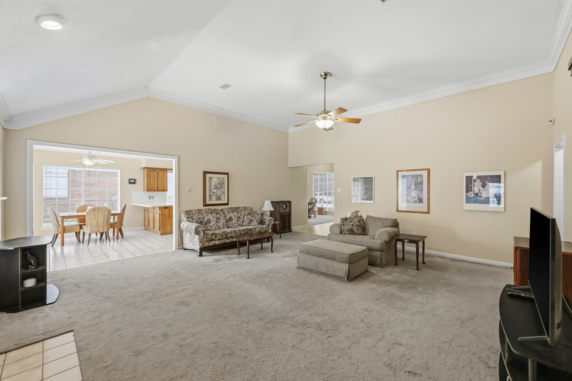 19806 Bambiwoods Court, Humble, TX 77346 This spacious living room features high ceilings, neutral walls, and carpeted flooring, creating a cozy atmosphere. It opens to a bright dining area with tile floors and large windows, offering a seamless flow for entertaining.