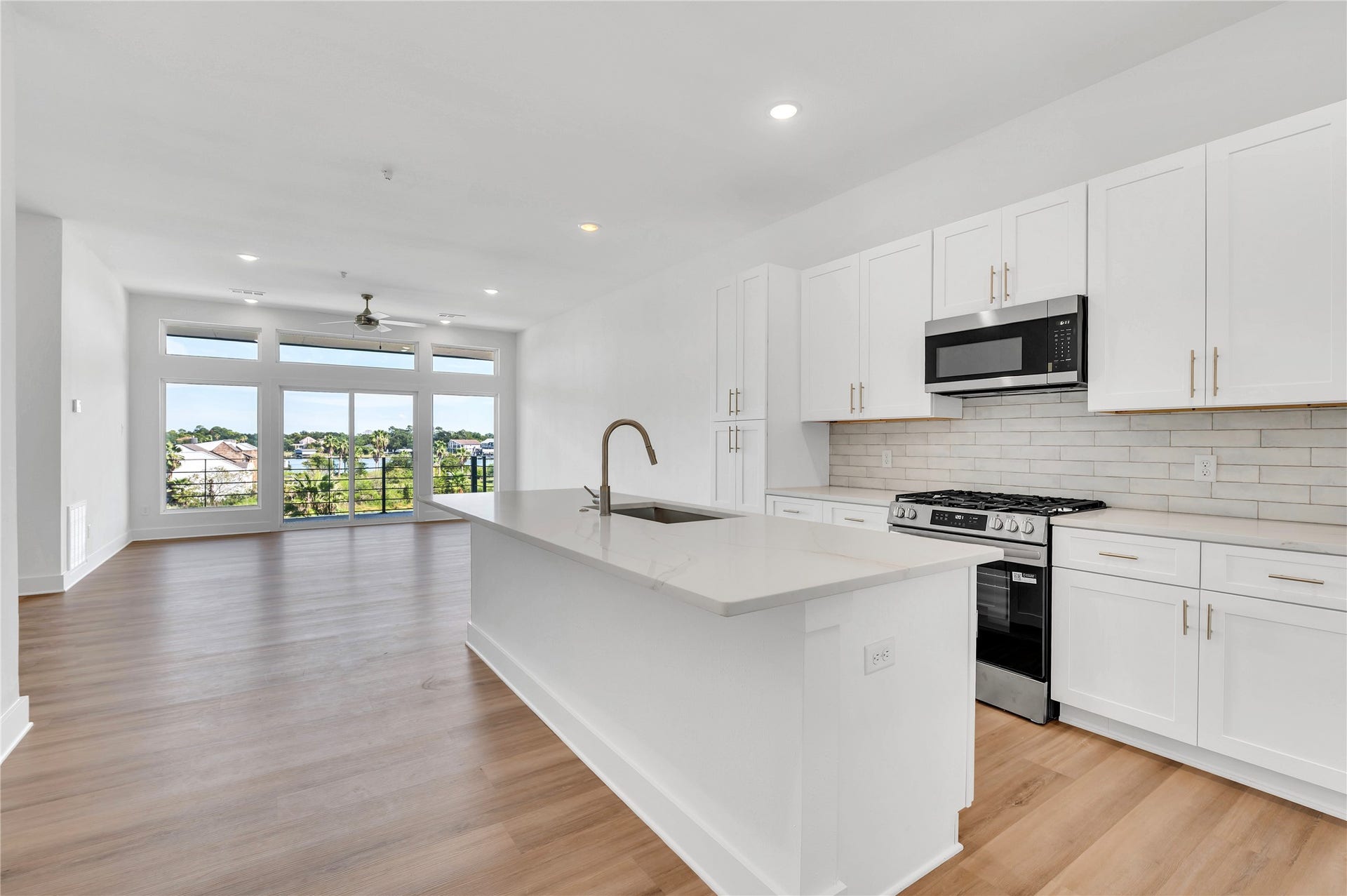 119 Kirby Road, #5201, Taylor Lake Village, TX 77586 Bright and modern open-concept kitchen and living area featuring sleek white cabinets, a central island, and large windows offering scenic views.