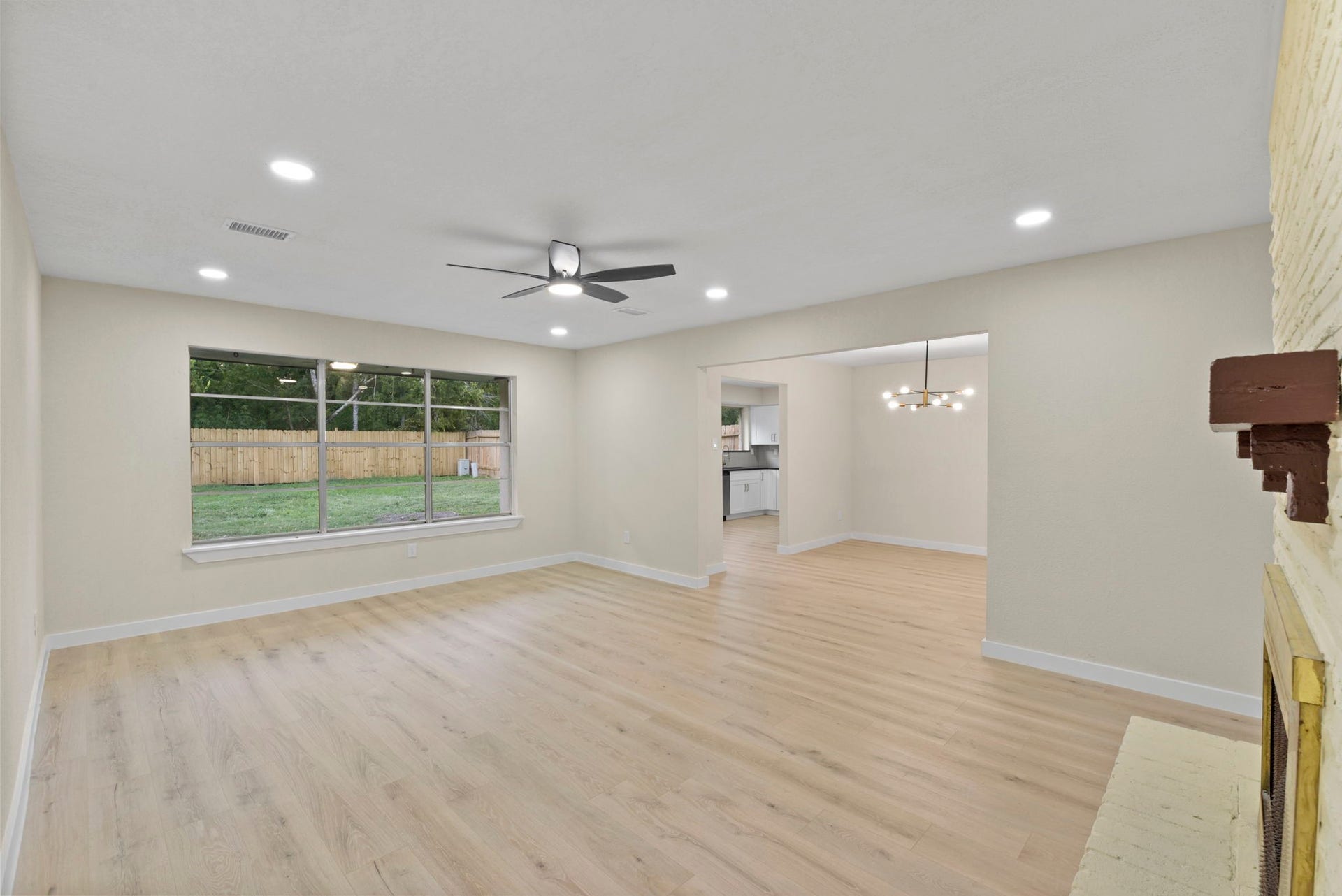 2322 Aprilmont Drive, Sugar Land, TX 77498 Spacious living area with hardwood floors, recessed lighting, and a cozy fireplace, seamlessly connecting to the dining and kitchen areas. Large windows offer abundant natural light and a view of the fenced backyard.
