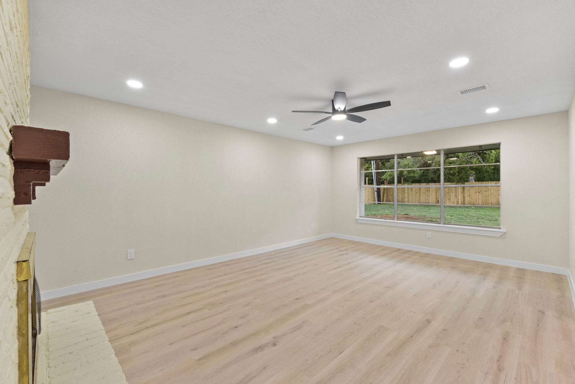 2322 Aprilmont Drive, Sugar Land, TX 77498 Bright, spacious living room with modern ceiling fan, large window overlooking the backyard, and elegant light wood flooring.