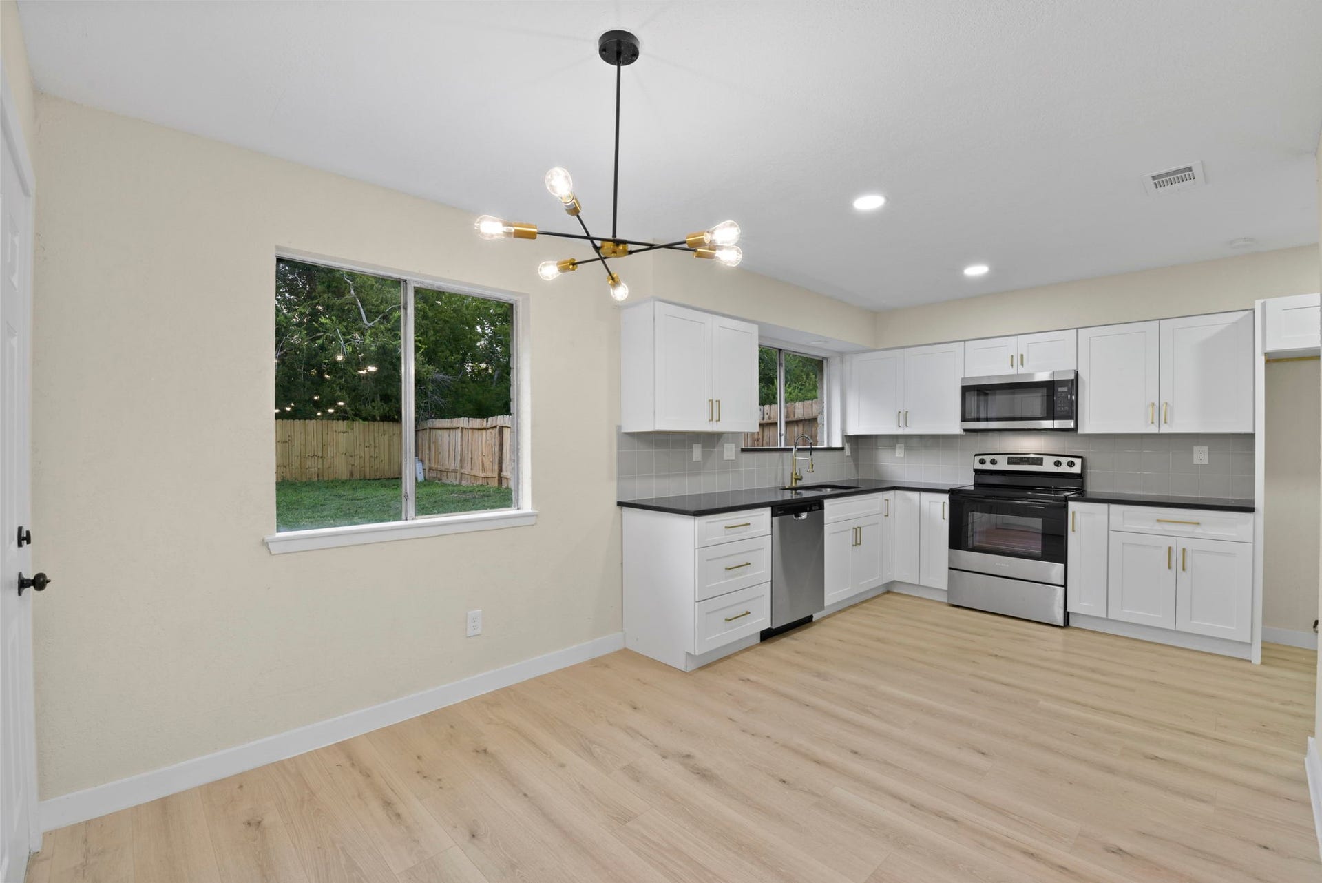 2322 Aprilmont Drive, Sugar Land, TX 77498 Bright, modern kitchen with sleek white cabinetry, stainless steel appliances, and a stylish light fixture, all complemented by light wood flooring and a large window offering a view of the backyard.