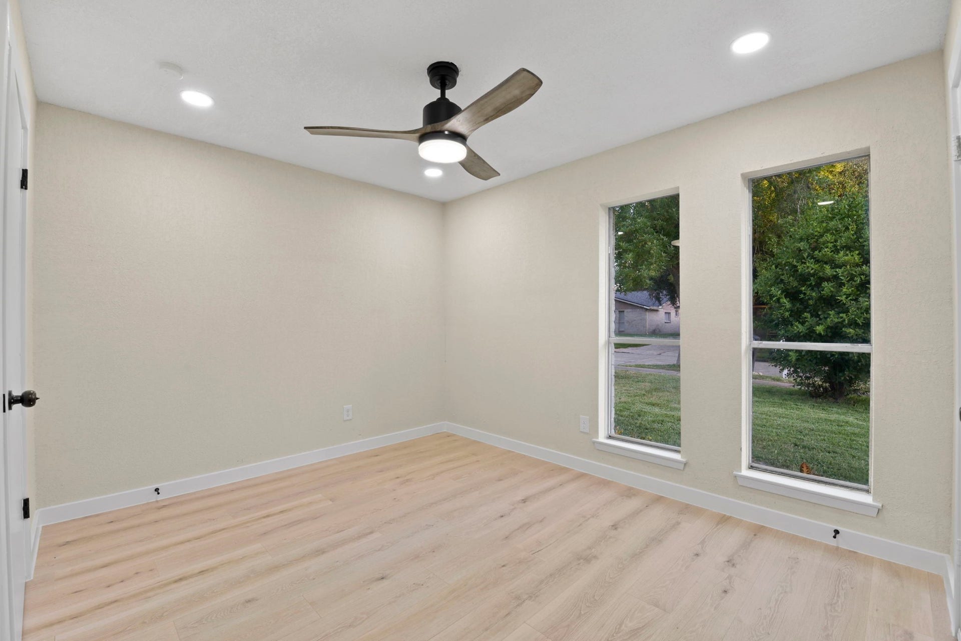 2322 Aprilmont Drive, Sugar Land, TX 77498 Bright and inviting room featuring sleek recessed lighting, a modern ceiling fan, and large windows that offer serene views of lush greenery, complemented by elegant light wood flooring.