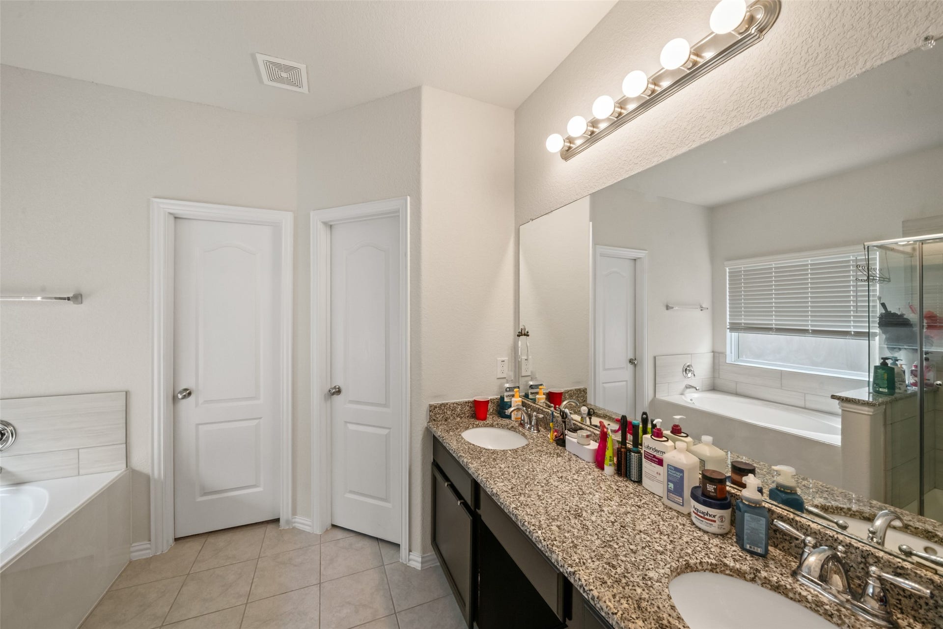 4509 Whitehaven Pine Way, Rosharon, TX 77583 Elegant bathroom featuring a granite double vanity, ample mirror space, and a luxurious soaking tub with natural light streaming in.