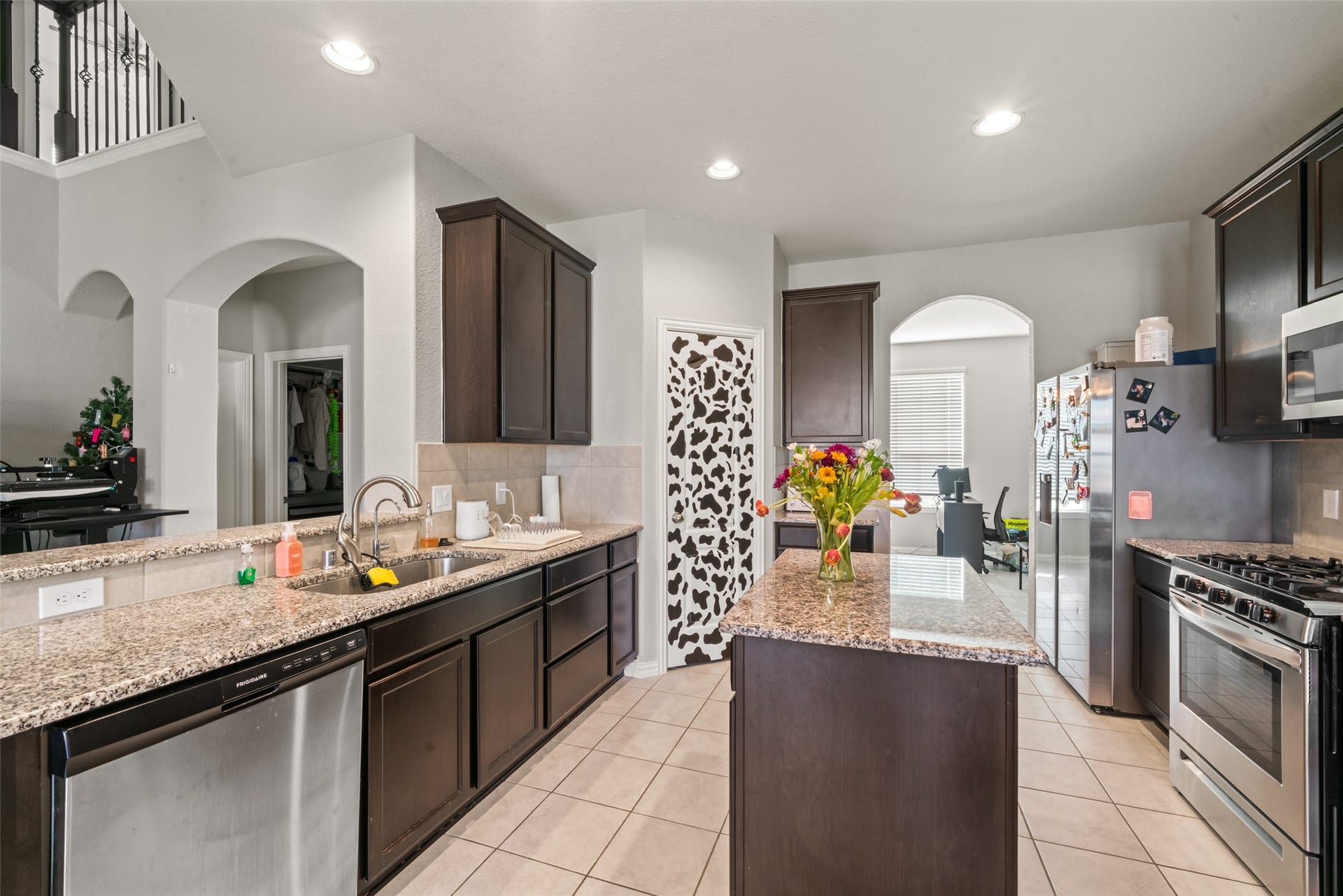 4509 Whitehaven Pine Way, Rosharon, TX 77583 Modern kitchen with granite countertops, stainless steel appliances, and dark wood cabinetry. An island with a floral centerpiece adds charm, while arched doorways provide an elegant touch.