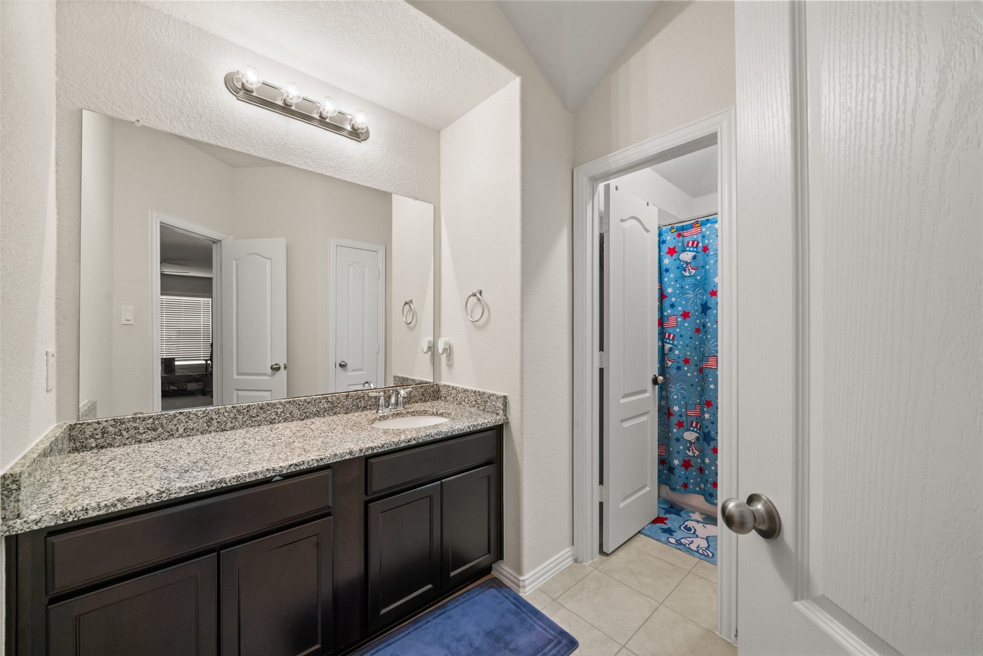 4509 Whitehaven Pine Way, Rosharon, TX 77583 Elegant bathroom featuring a granite countertop, dark wood cabinetry, and a spacious mirror, leading to a charming shower area.