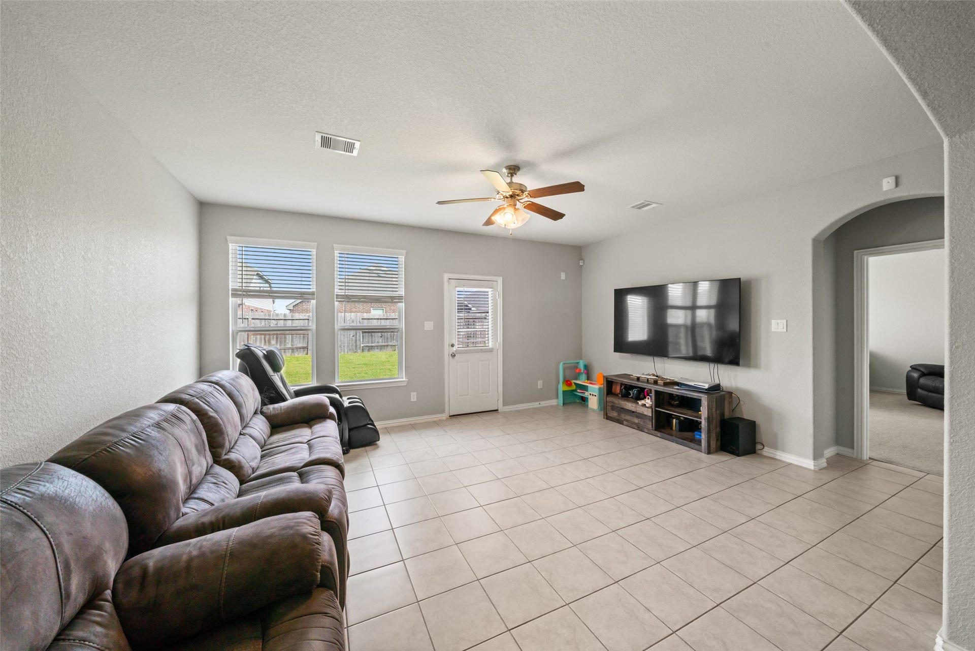 4509 Whitehaven Pine Way, Rosharon, TX 77583 Spacious living room with a tiled floor, featuring a cozy reclining sofa and large windows offering plenty of natural light.