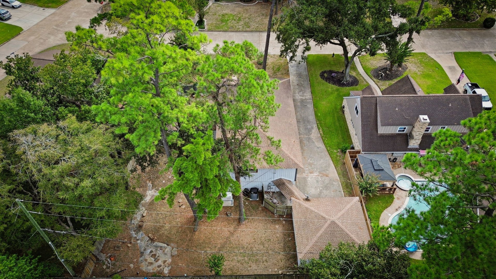 Property nestled among greenery and trees, featuring a driveway to a detached garage and inviting backyard.