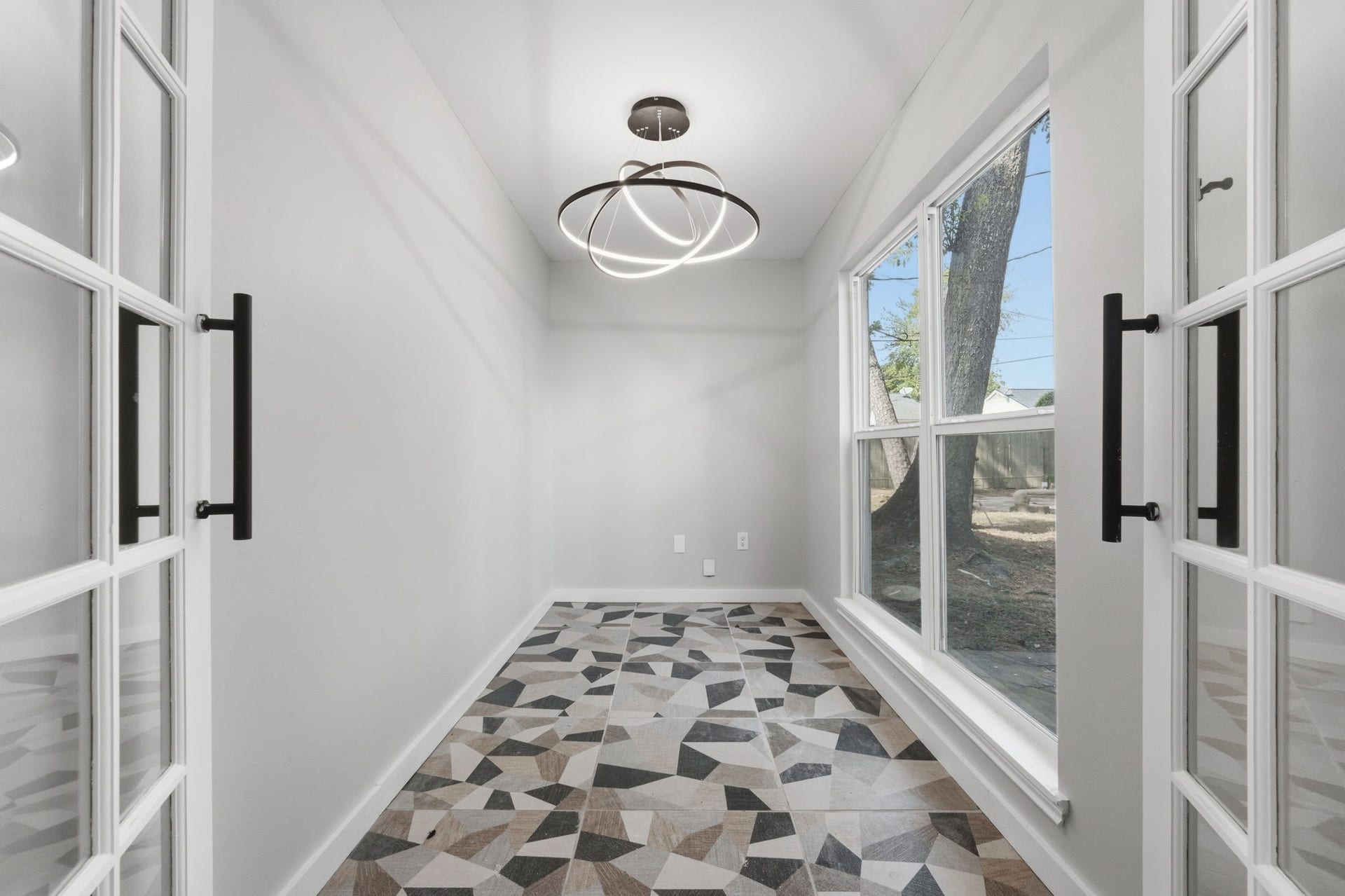 This quaint study features large windows and french doors with modern geometric flooring.