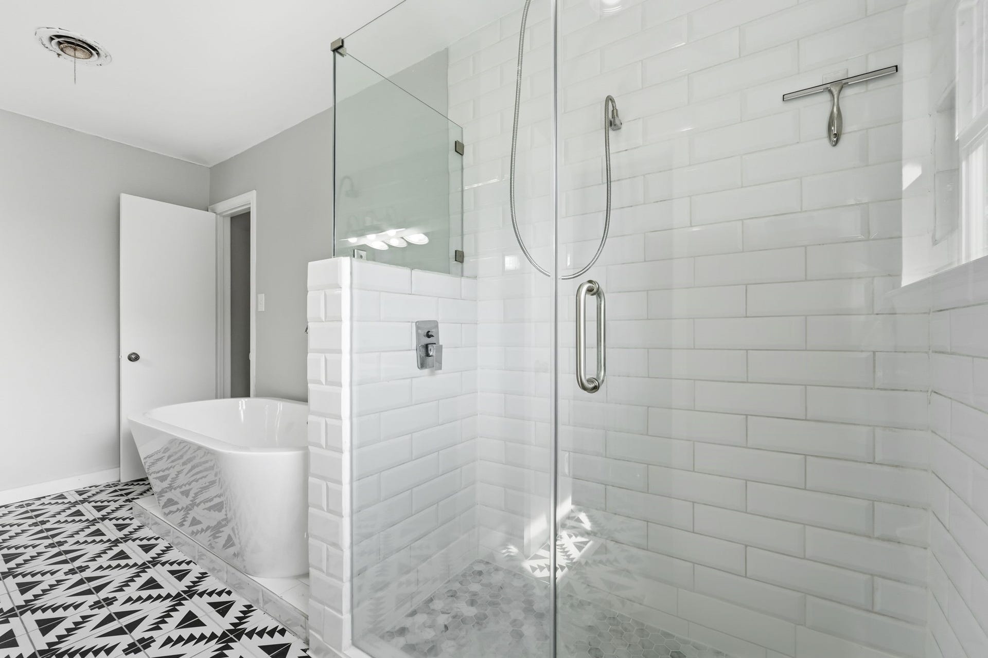 Bright and modern bathroom featuring a large glass shower and a stylish freestanding bathtub complemented by patterned floor tiles.