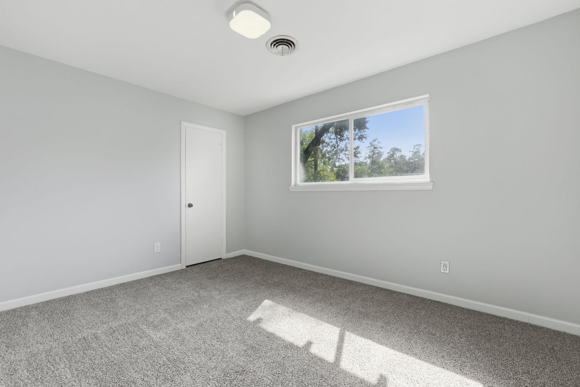 Bright bedroom with plush carpet and a large window.