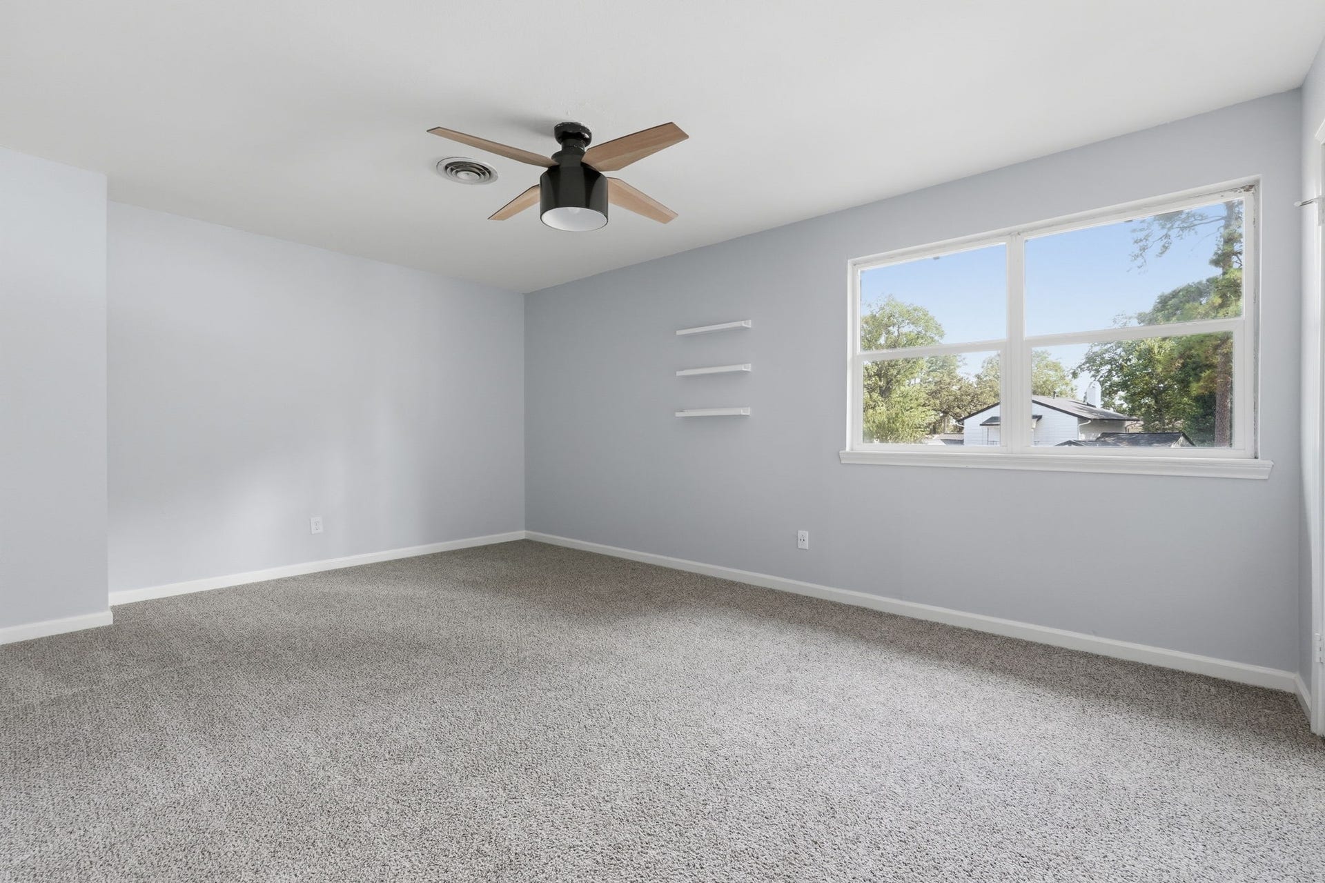 Spacious and bright bedroom with soft carpet, a large window for natural light, and a modern ceiling fan.