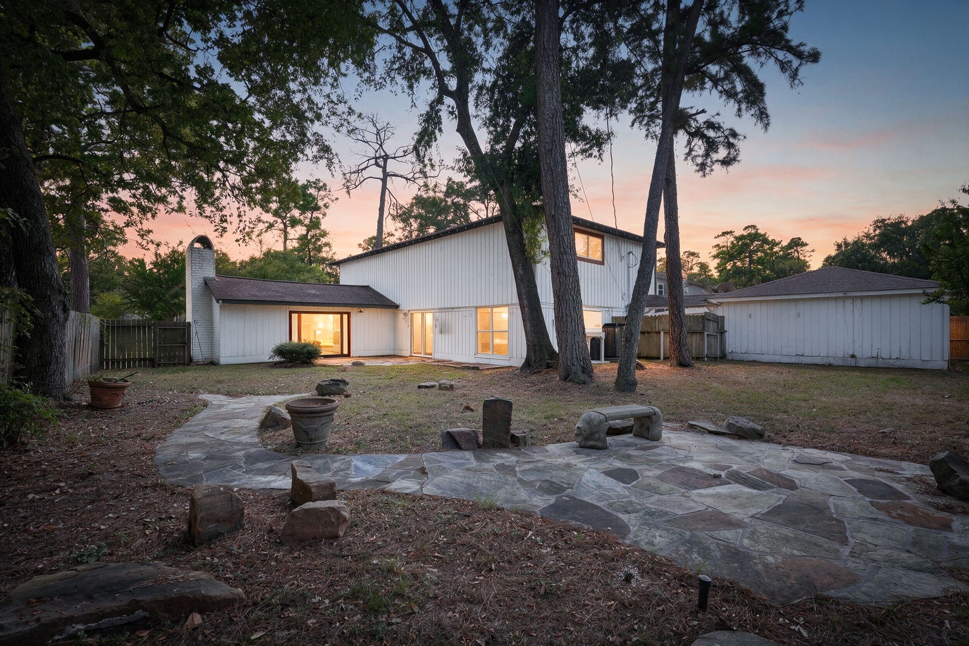 Charming two-story home with a spacious backyard, featuring a stone patio and surrounded by trees, perfect for outdoor gatherings.