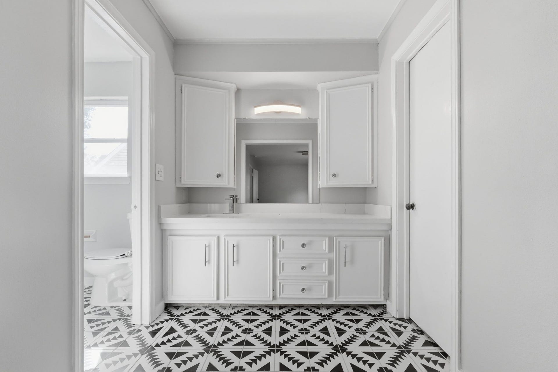Bright bathroom featuring a sleek white vanity with ample storage, illuminated by modern lighting, and newly furnished tiles.