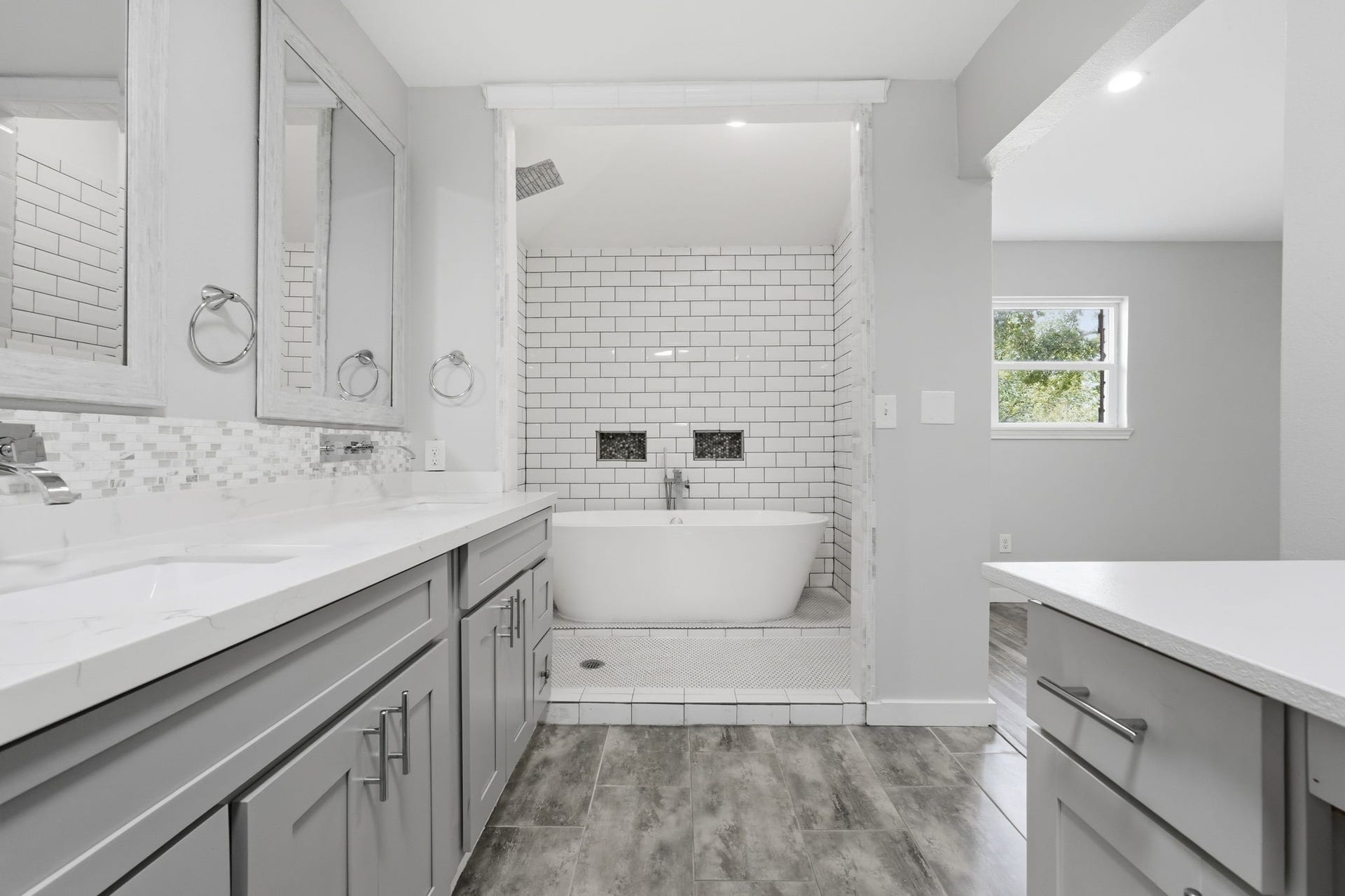 This luxurious bathroom features a freestanding, soaking bathtub framed by elegant white subway tiles and a large rainfall shower.