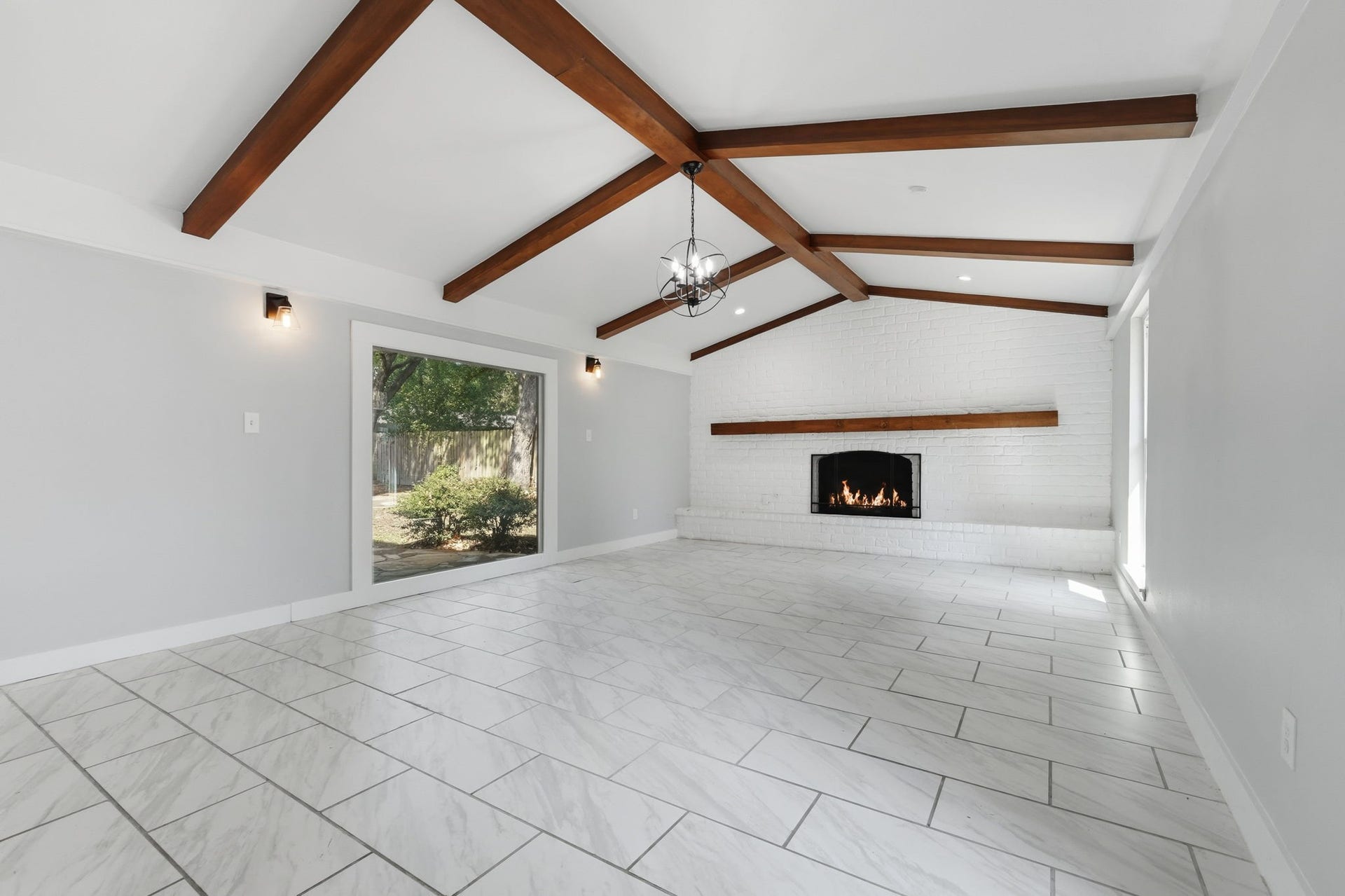 This large living room with an elegant wood-beamed ceiling and a cozy fireplace creates the perfect warm and inviting atmosphere.