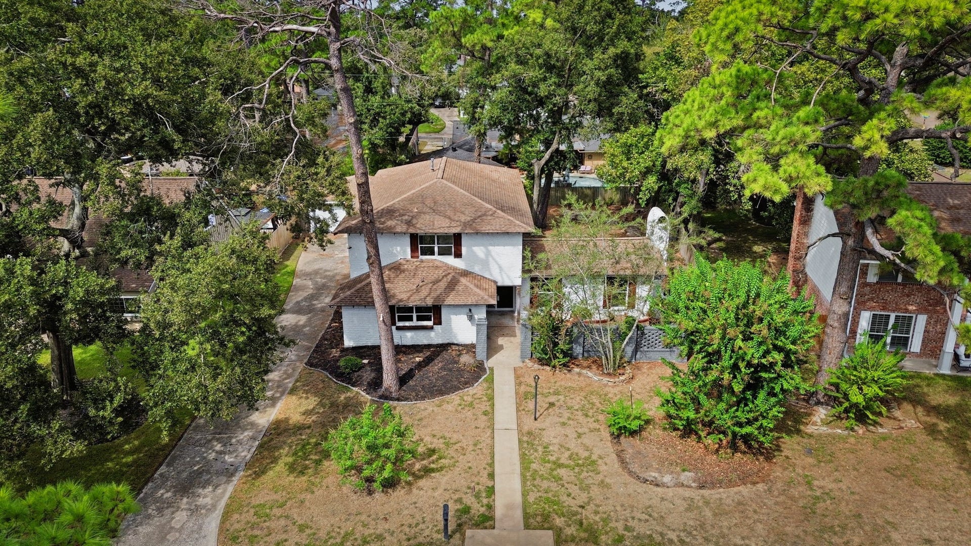 Charming two-story home nestled among many trees, featuring a welcoming path to the entrance and a spacious front yard.