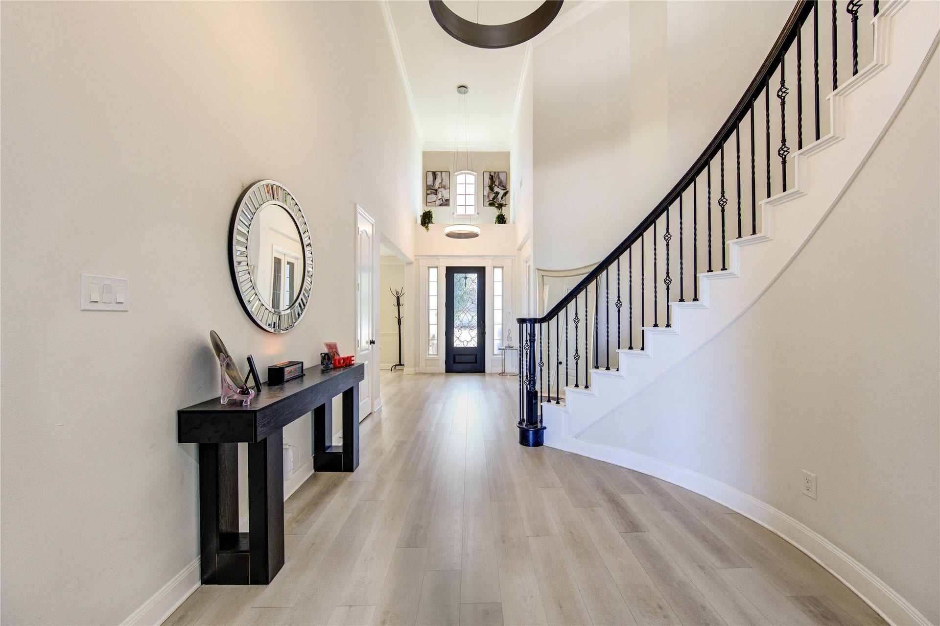 Impressive entryway with soaring ceilings and an abundance of natural light, creating a bright and welcoming first impression. The elegant staircase with wrought iron balusters adds a touch of sophistication, while the light  flooring enhances the open and airy feel. A stylish console table and modern finishes complete this beautifully designed space, setting the tone for the rest of the home.