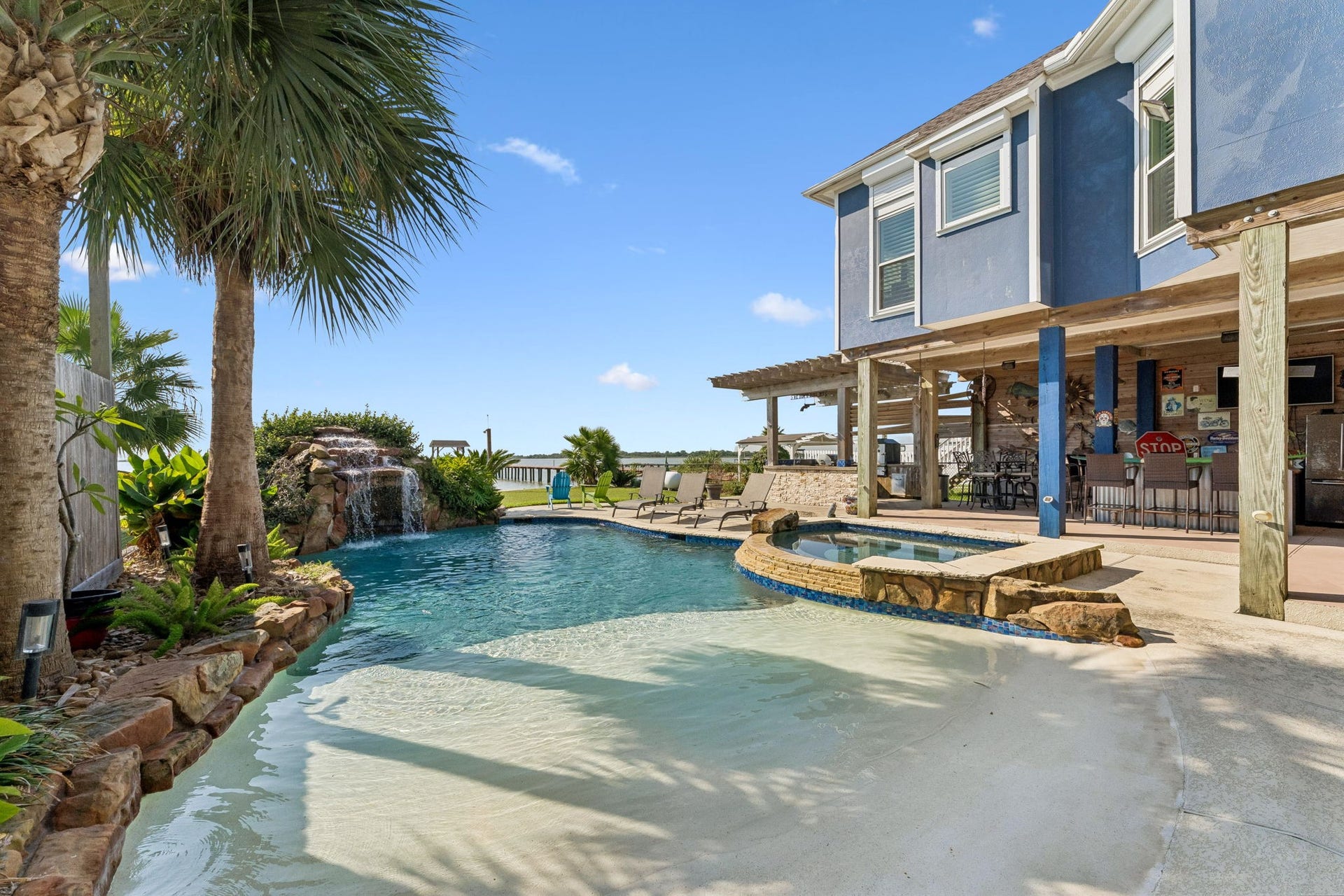 1623 Dick Bay Drive, San Leon, TX 77539 Resort-style pool with a built-in hot tub, waterfall feature, and lush tropical landscaping. The covered outdoor kitchen and bar create the perfect setting for poolside entertaining