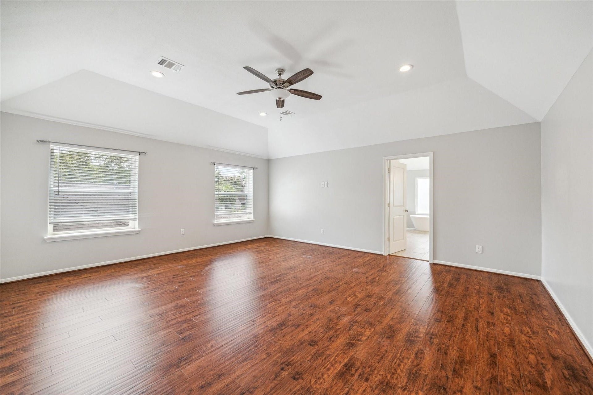 6003 Ancient Oaks Drive, Humble, TX 77346 Generously sized primary bedroom featuring warm wood-look flooring, a ceiling fan, multiple windows, and plenty of room for a complete bedroom setup.