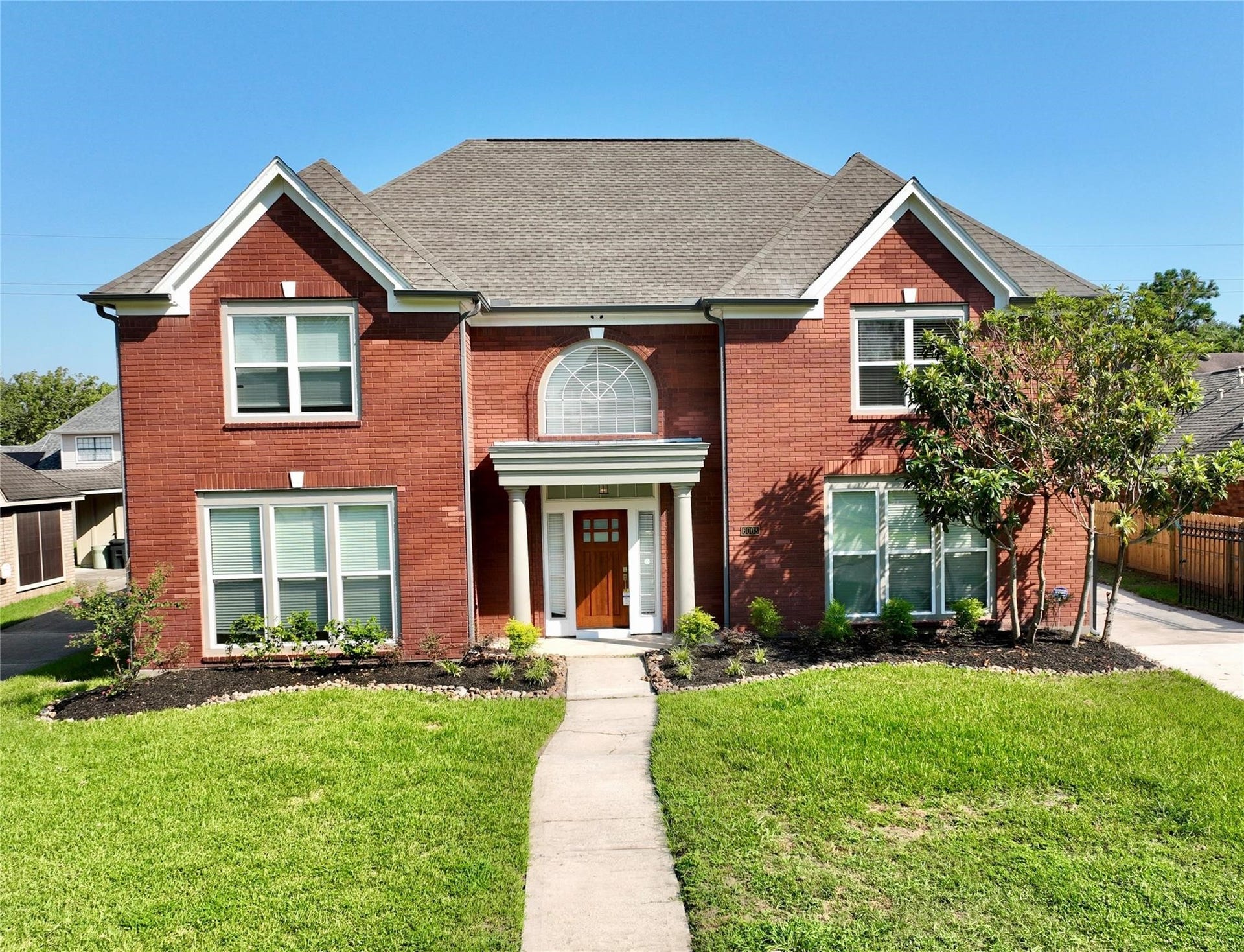 6003 Ancient Oaks Drive, Humble, TX 77346 Front view of the beautifully remodeled two-story brick home, featuring a spacious lawn, mature landscaping, and a welcoming covered entry.