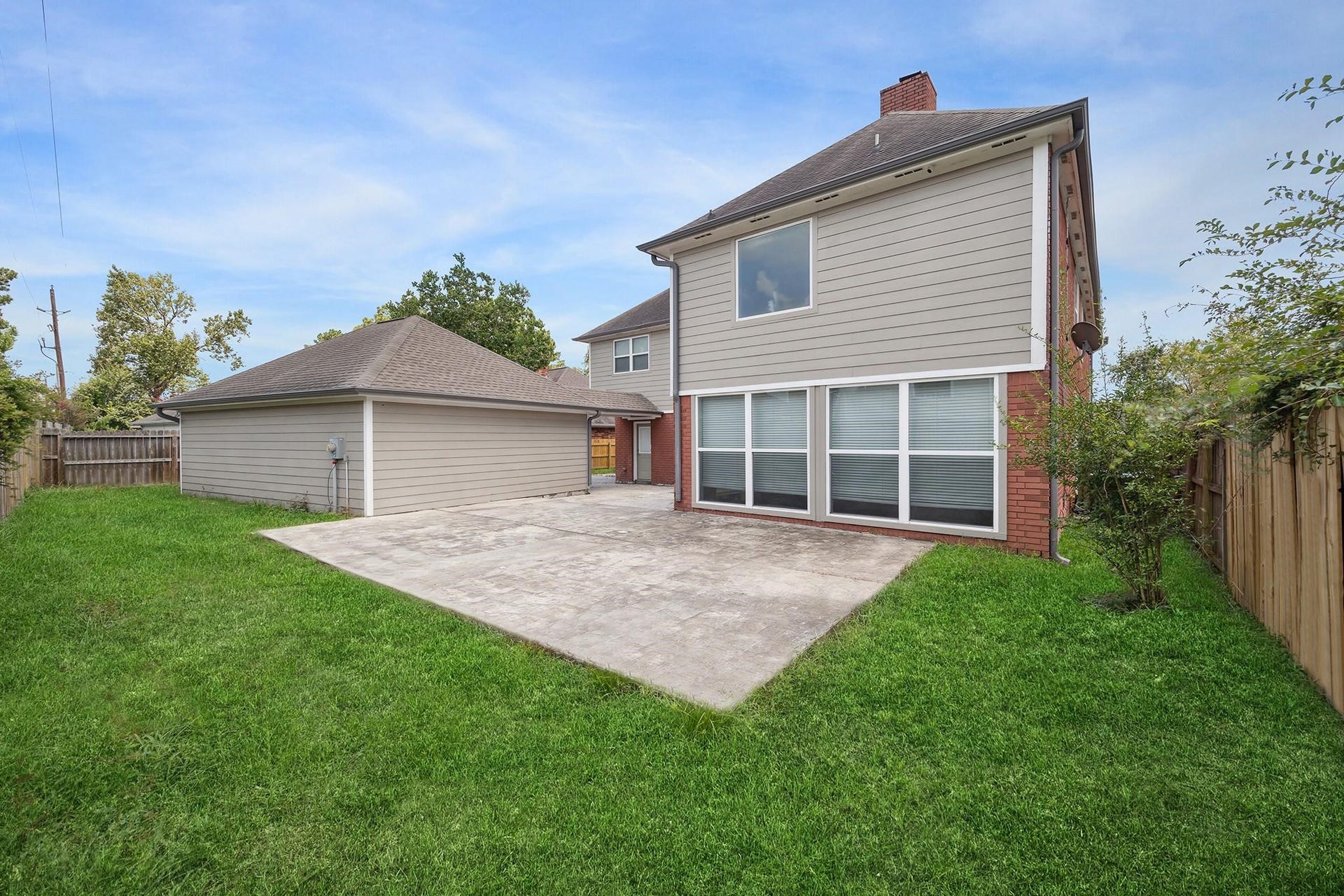 6003 Ancient Oaks Drive, Humble, TX 77346 Rear exterior view featuring a fenced backyard, open lawn, paved patio area, and detached garageideal for relaxing or outdoor entertaining.