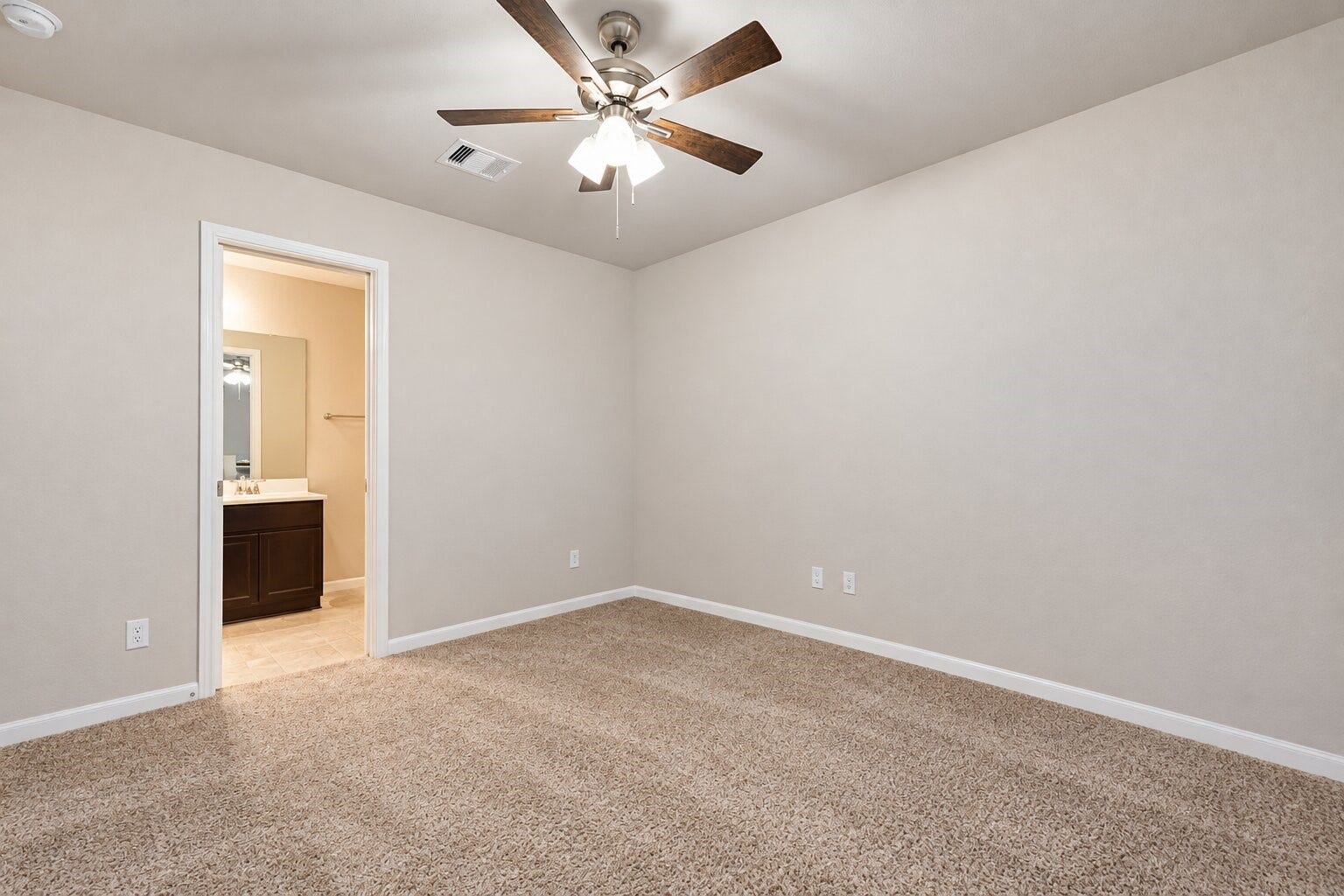 Versatile bedroom featuring neutral walls, plush carpeting, a ceiling fan with lighting, and convenient access to an adjoining bathroom. A flexible space ready to accommodate a variety of furniture arrangements. Photo has been digitally decluttered.