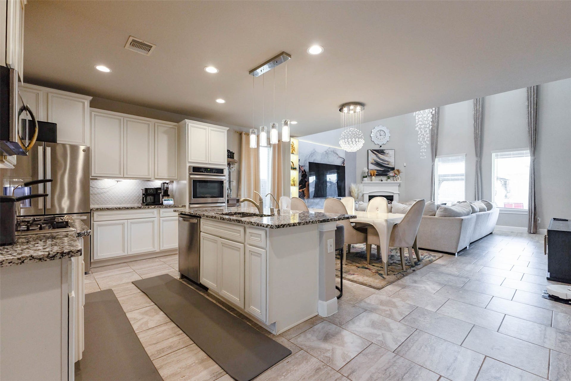 A corner view of the kitchen shows the cooktop and wall oven, the large island with a sink and a stainless dishwasher, and a long run of white cabinetry. Granite countertops continue around the room, and the pendant lights over the island add a decorative touch. The kitchen opens to the dining area and the family room, so the cook can see everyone and everything at once. It is a great layout for entertaining.