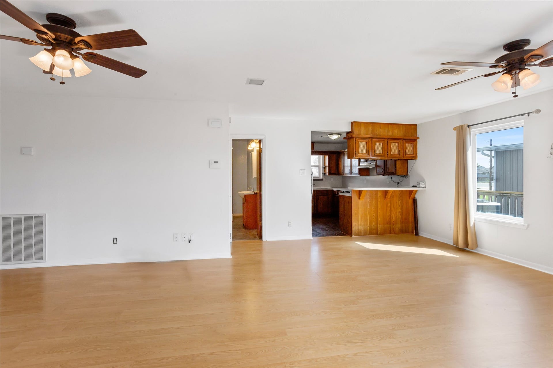 31 Lakeside Drive, Hitchcock, TX 77563 This spacious, light-filled living area features wood laminate flooring, ceiling fans, and a large window. It seamlessly connects to an open kitchen with wooden cabinetry and a breakfast bar, creating a warm and inviting atmosphere.