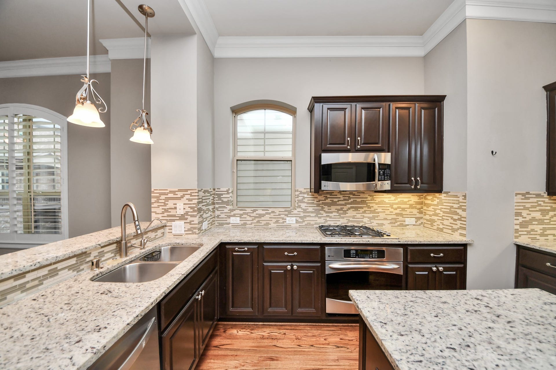 1617 W 23rd Street, Houston, TX 77008 Elegant kitchen featuring dark wood cabinetry, granite countertops, and modern stainless steel appliances, complemented by a stylish tile backsplash.