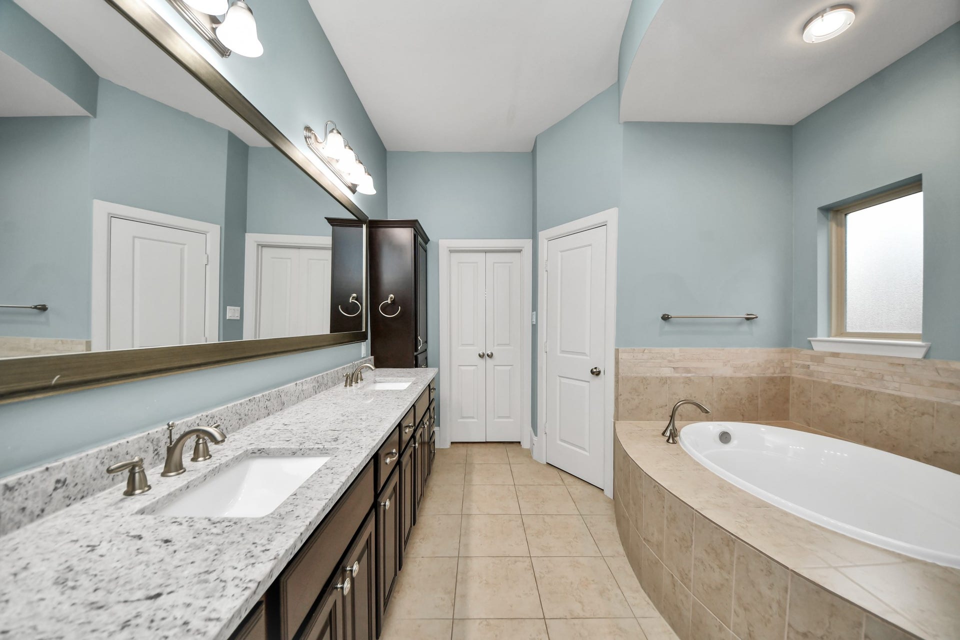 1617 W 23rd Street, Houston, TX 77008 Experience luxury in the primary bathroom, featuring a spacious dual-sink vanity, elegant granite countertops, and a relaxing soaking tub surrounded by serene blue walls.