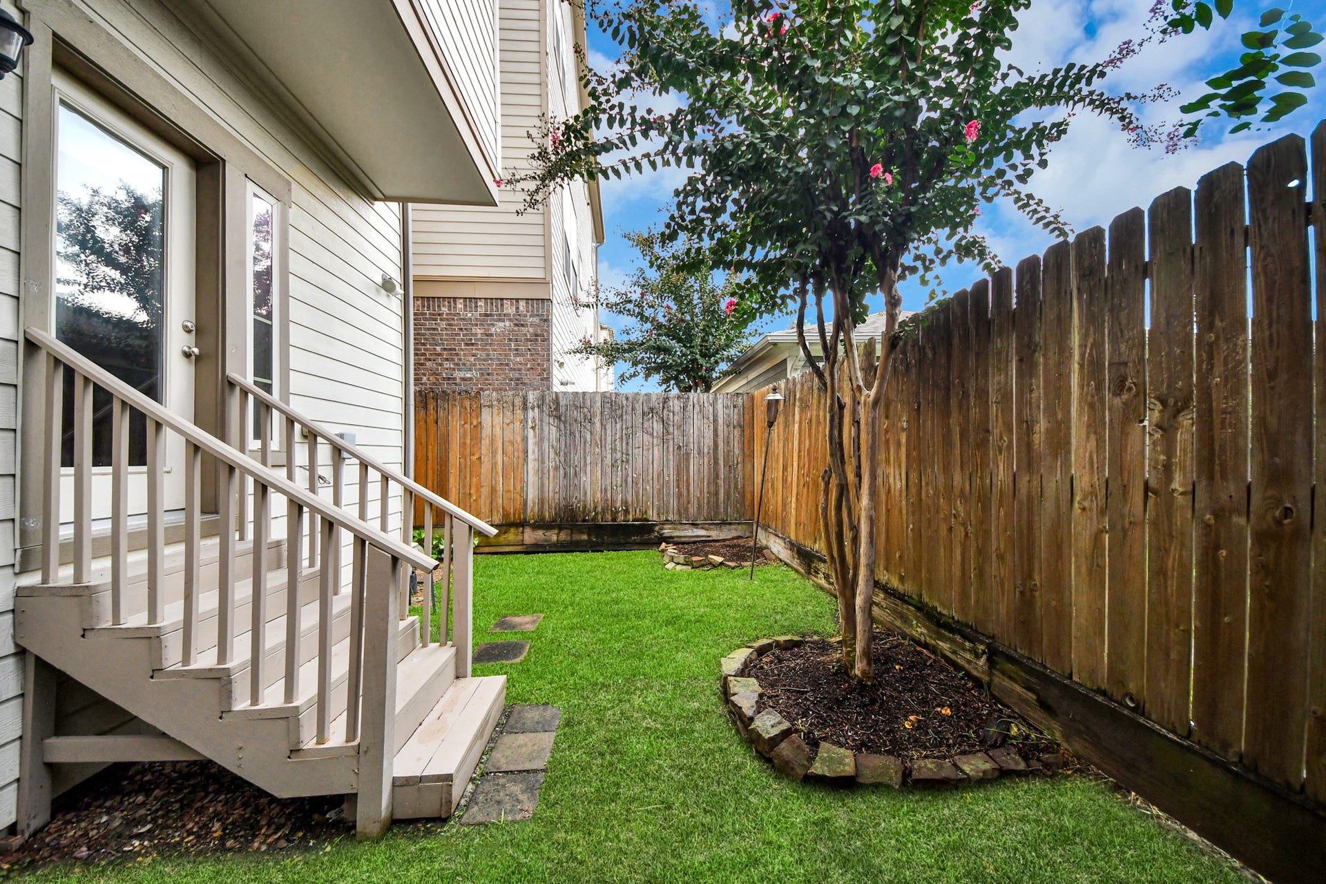 1617 W 23rd Street, Houston, TX 77008 Charming backyard space with lush green grass, a blooming tree, and a privacy fence, perfect for relaxing or entertaining.