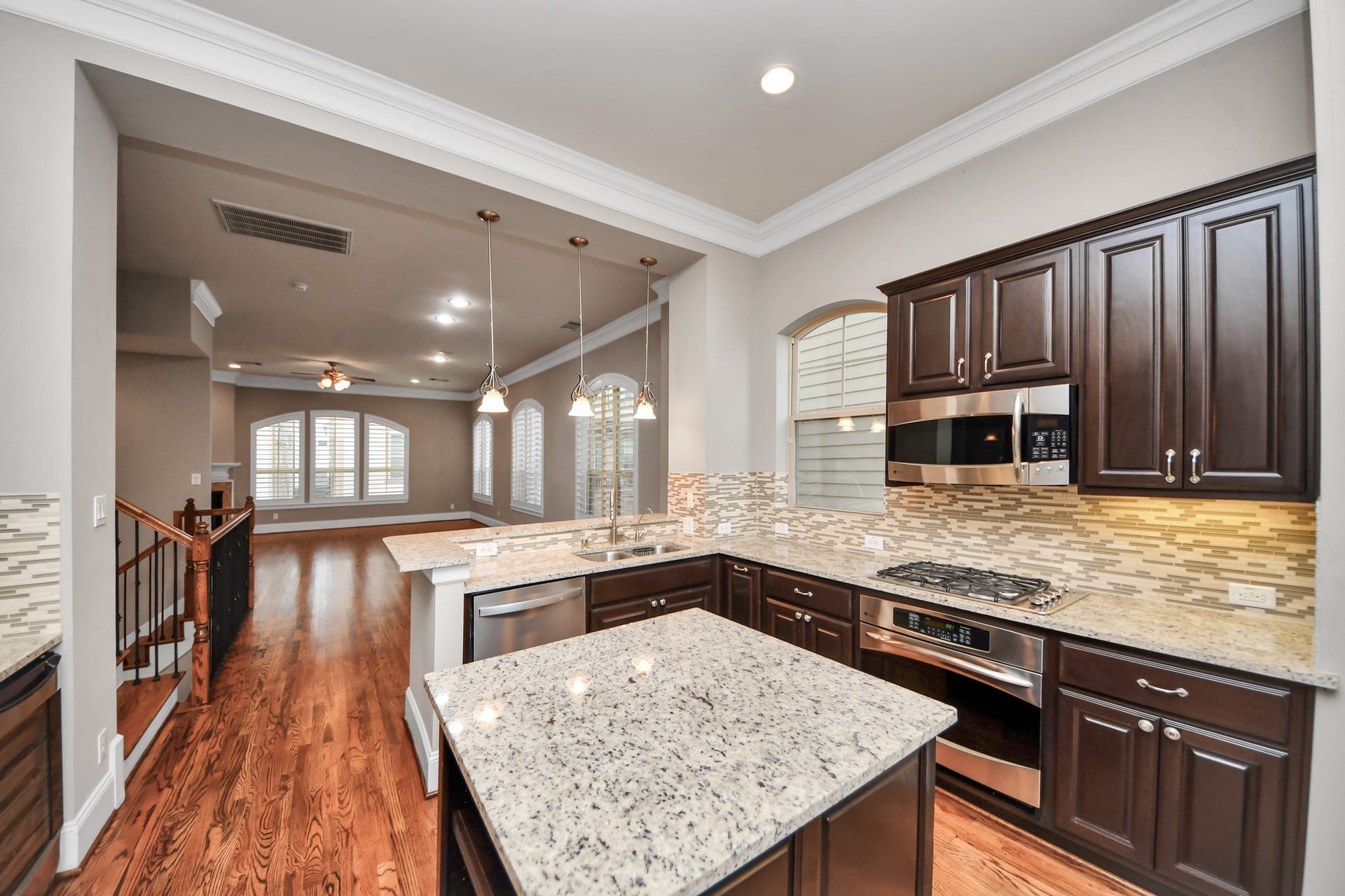 1617 W 23rd Street, Houston, TX 77008 Elegant open-concept kitchen with rich wood cabinetry, granite countertops, and stainless steel appliances, seamlessly flowing into a spacious living area with hardwood floors and large arched windows.