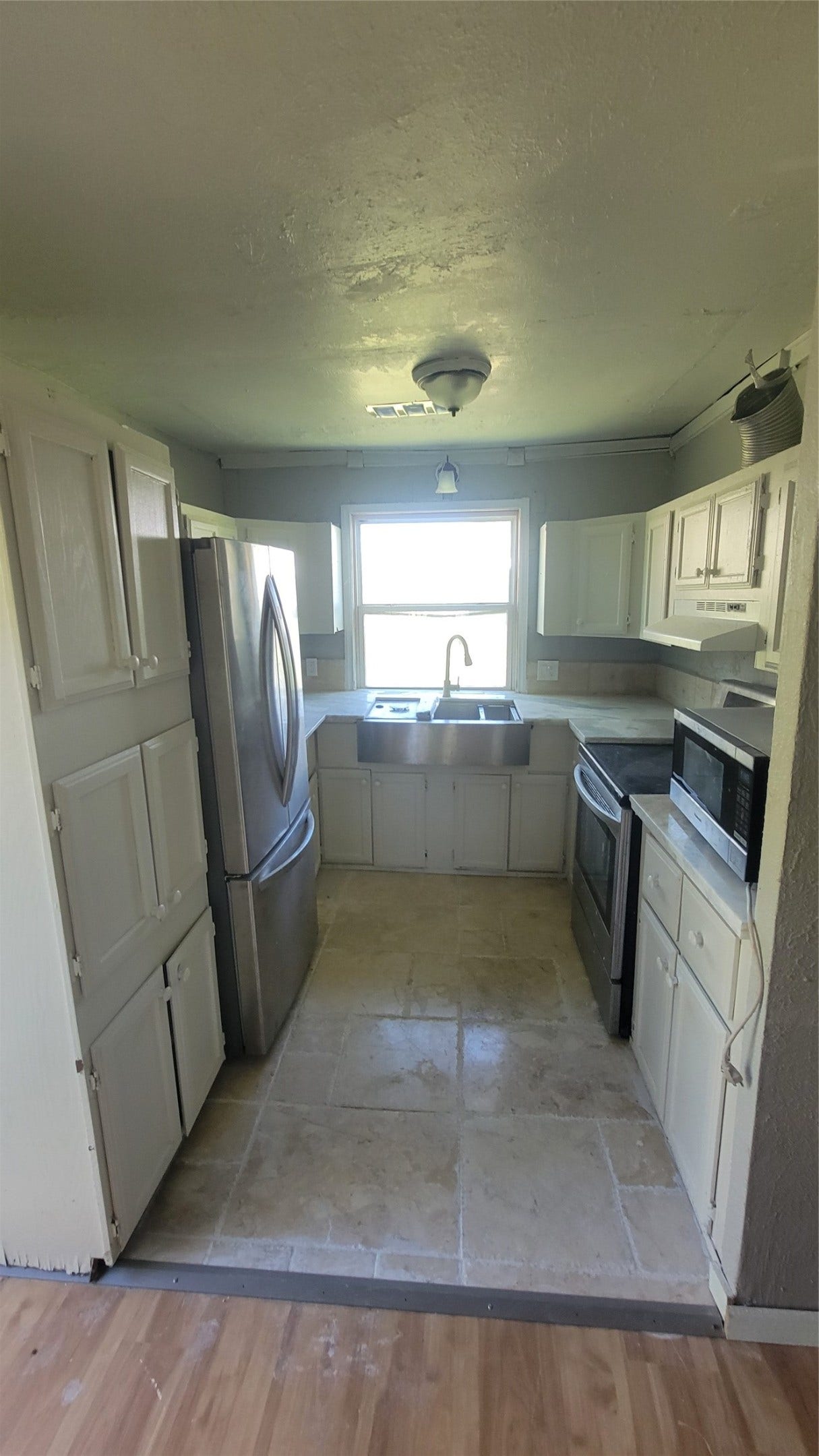12018 Sandpiper Road, Angleton, TX 77515 This compact kitchen features stainless steel appliances, white cabinetry, and tile flooring. A large window above the sink provides natural light, creating a bright and functional space.