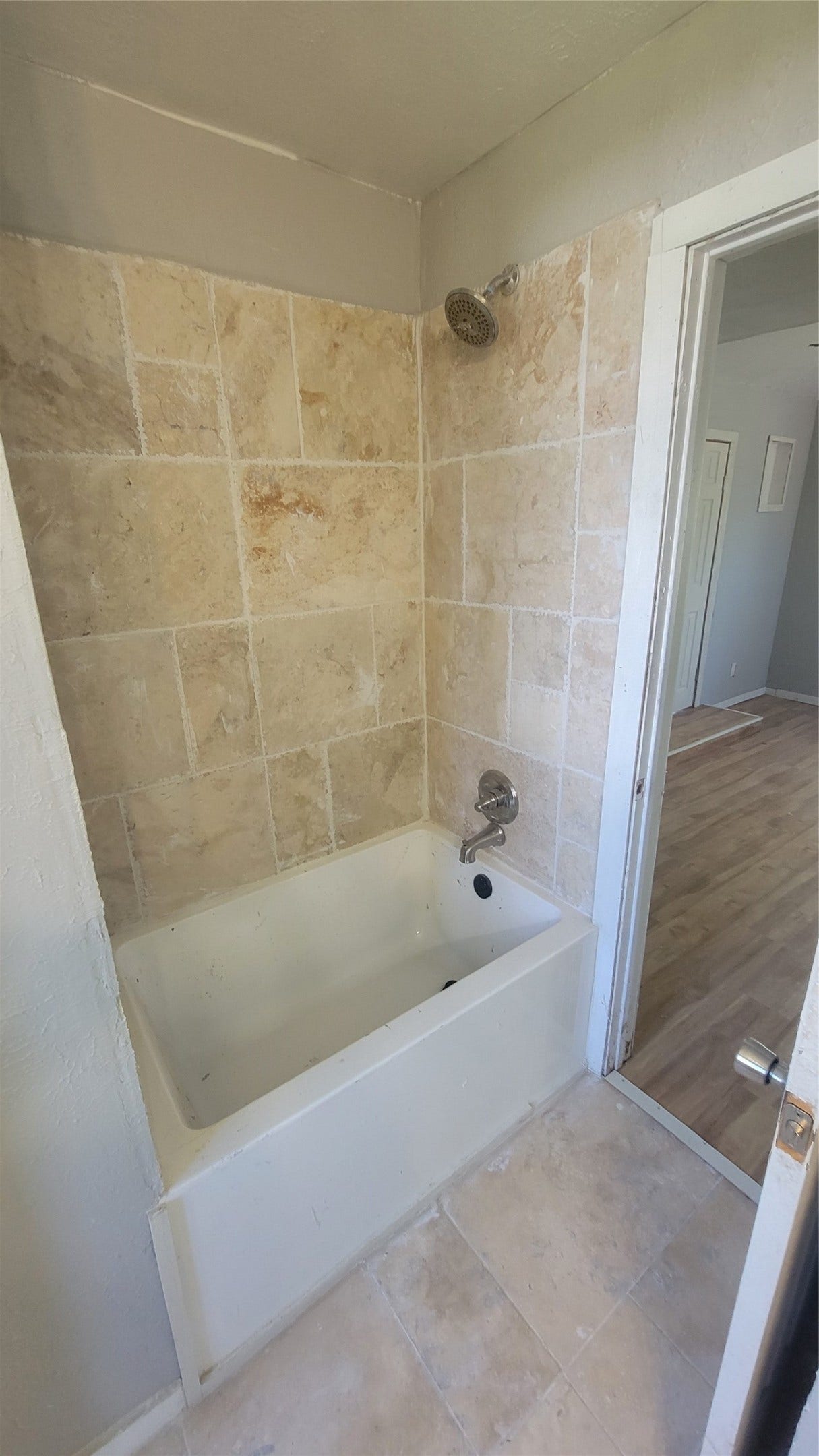 12018 Sandpiper Road, Angleton, TX 77515 This bathroom features a clean, classic bathtub with a tiled surround in neutral tones and a matching floor. It opens into a room with hardwood flooring, offering a cozy and practical space.