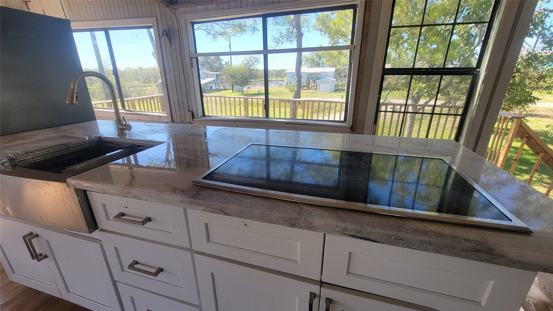 12018 Sandpiper Road, Angleton, TX 77515 This kitchen features a modern cooktop set in a sleek marble countertop alongside a stylish sink. Large windows provide abundant natural light and offer a scenic view of the outdoor greenery.