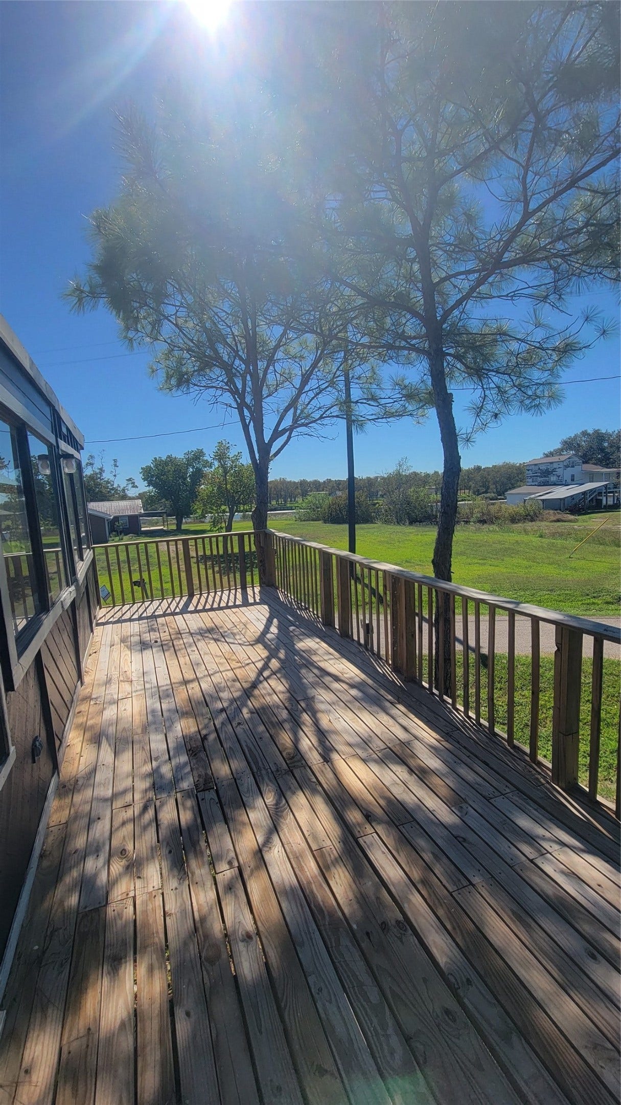12018 Sandpiper Road, Angleton, TX 77515 This photo showcases a spacious wooden deck with railing, surrounded by lush greenery and mature trees, offering a serene view of the surrounding area. Perfect for outdoor relaxation and entertaining.