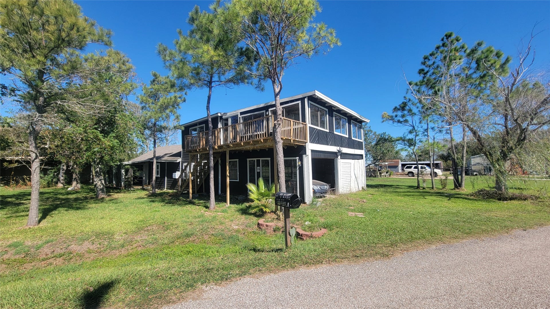 12018 Sandpiper Road, Angleton, TX 77515 This photo shows a two-story home with a wooden balcony on the upper level, surrounded by trees and grassy areas. The house features a garage and a driveway, set in a quiet, sunny neighborhood.