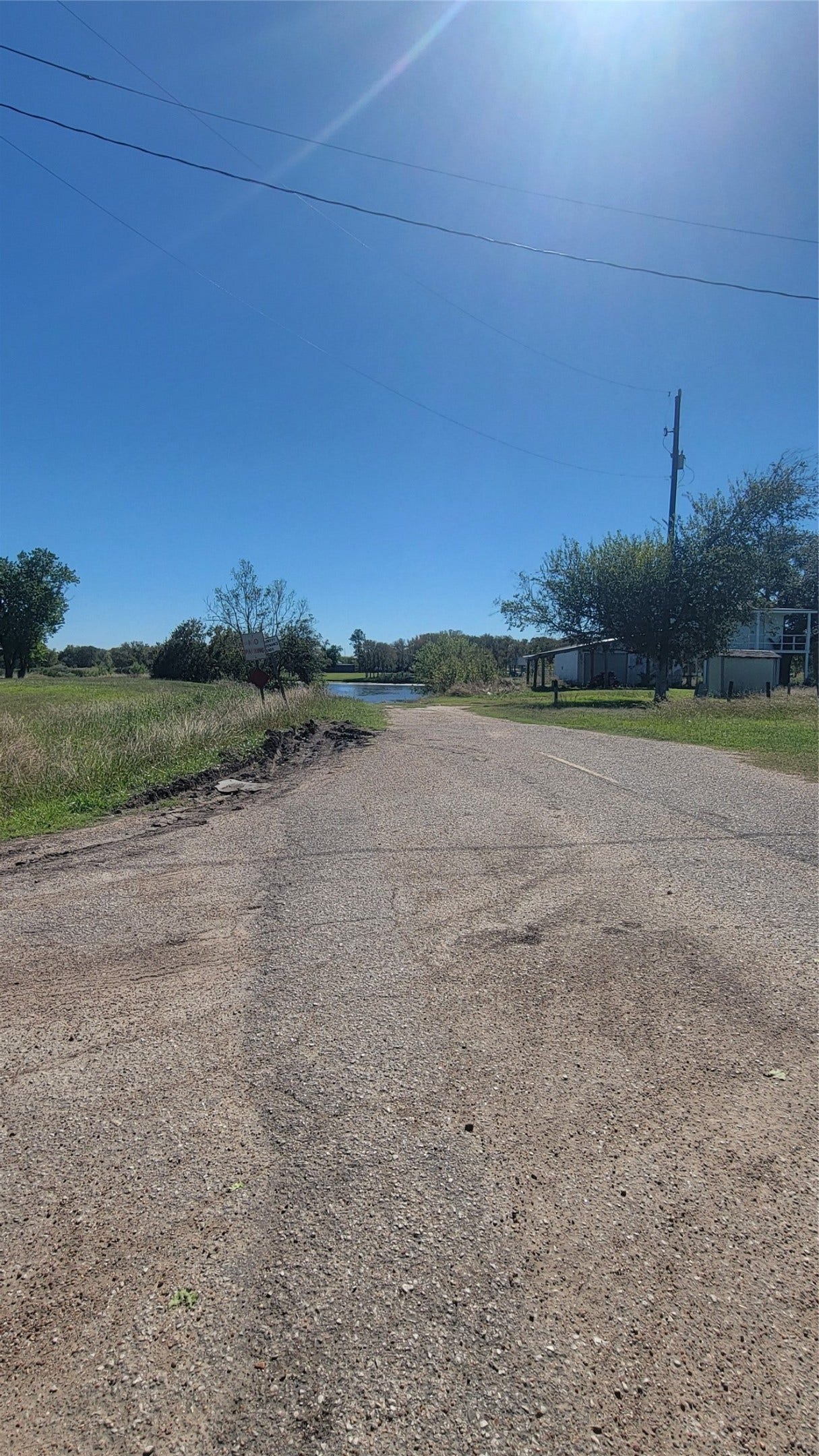 12018 Sandpiper Road, Angleton, TX 77515 A quiet, rural road with open fields on either side and a clear blue sky. There are a few trees and a glimpse of a house to the right, offering a peaceful, country living vibe.