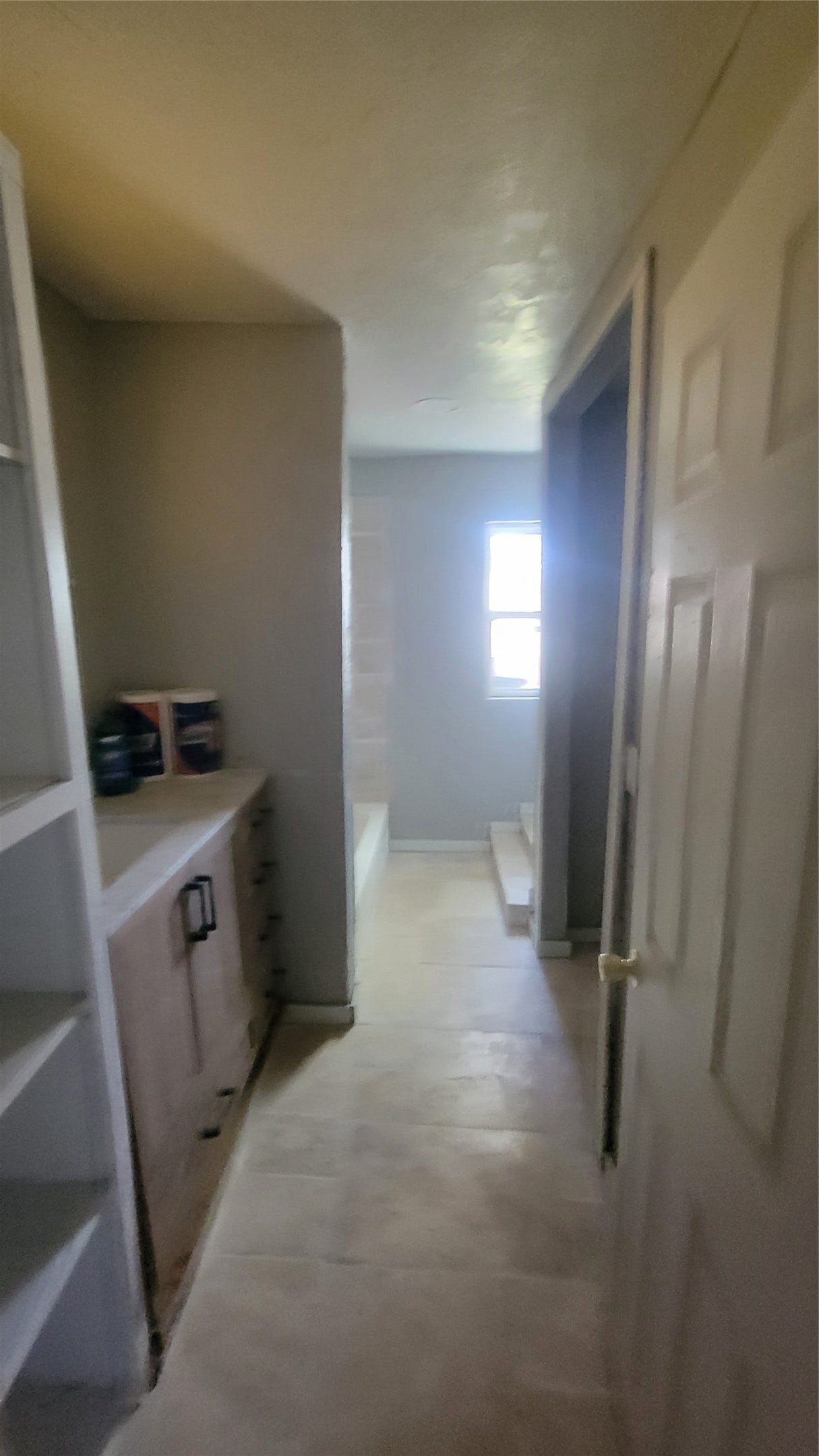 12018 Sandpiper Road, Angleton, TX 77515 This photo shows a narrow hallway leading to a bathroom with a window. The space includes built-in shelving and a countertop, with light-colored flooring and a neutral color scheme.