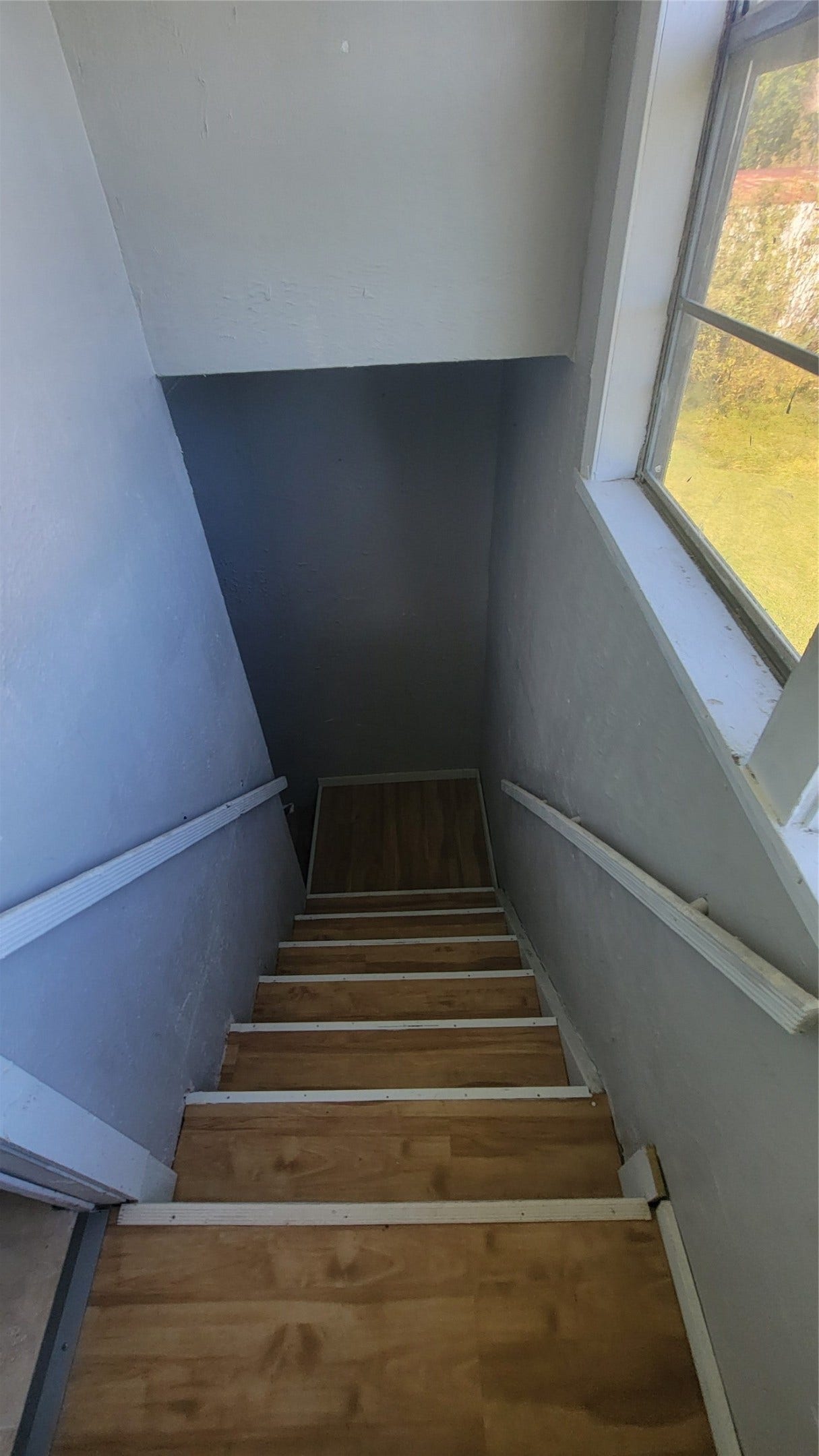 12018 Sandpiper Road, Angleton, TX 77515 This photo shows a narrow staircase with wooden steps and white handrails, leading down to a lower level. There's a window on the right, providing natural light.