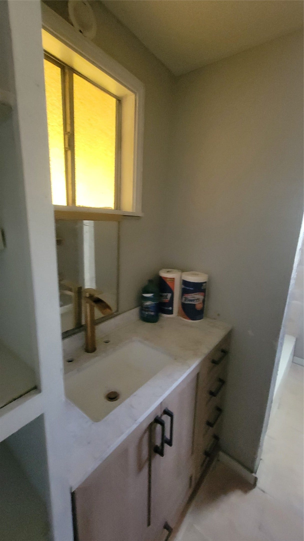 12018 Sandpiper Road, Angleton, TX 77515 This photo shows a compact bathroom area featuring a sink with a marble countertop, modern brass faucet, and under-sink storage. A small window provides natural light, and there's shelving for additional storage.