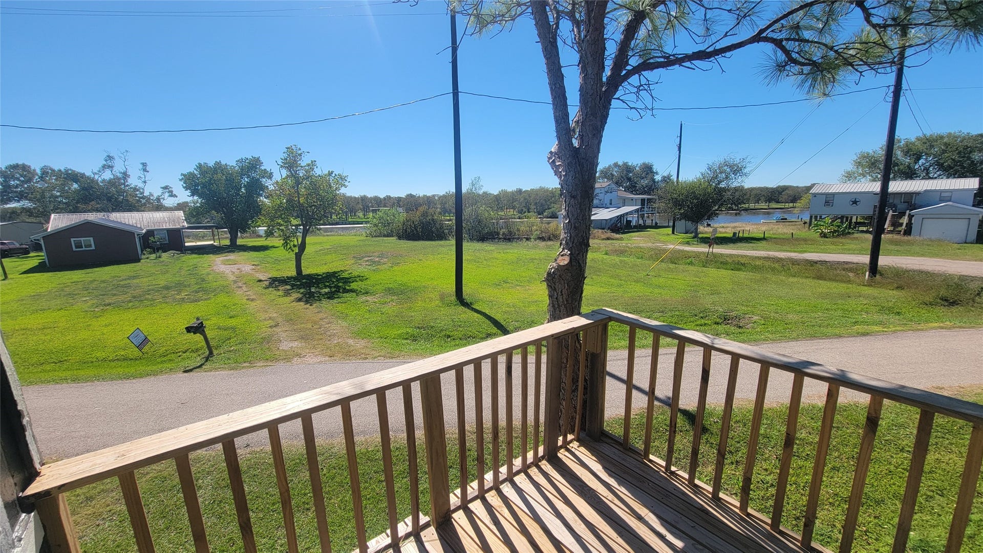 12018 Sandpiper Road, Angleton, TX 77515 Charming neighborhood view from a cozy wooden balcony, overlooking a grassy area with a clear sky and nearby houses. Ideal for enjoying peaceful outdoor moments.