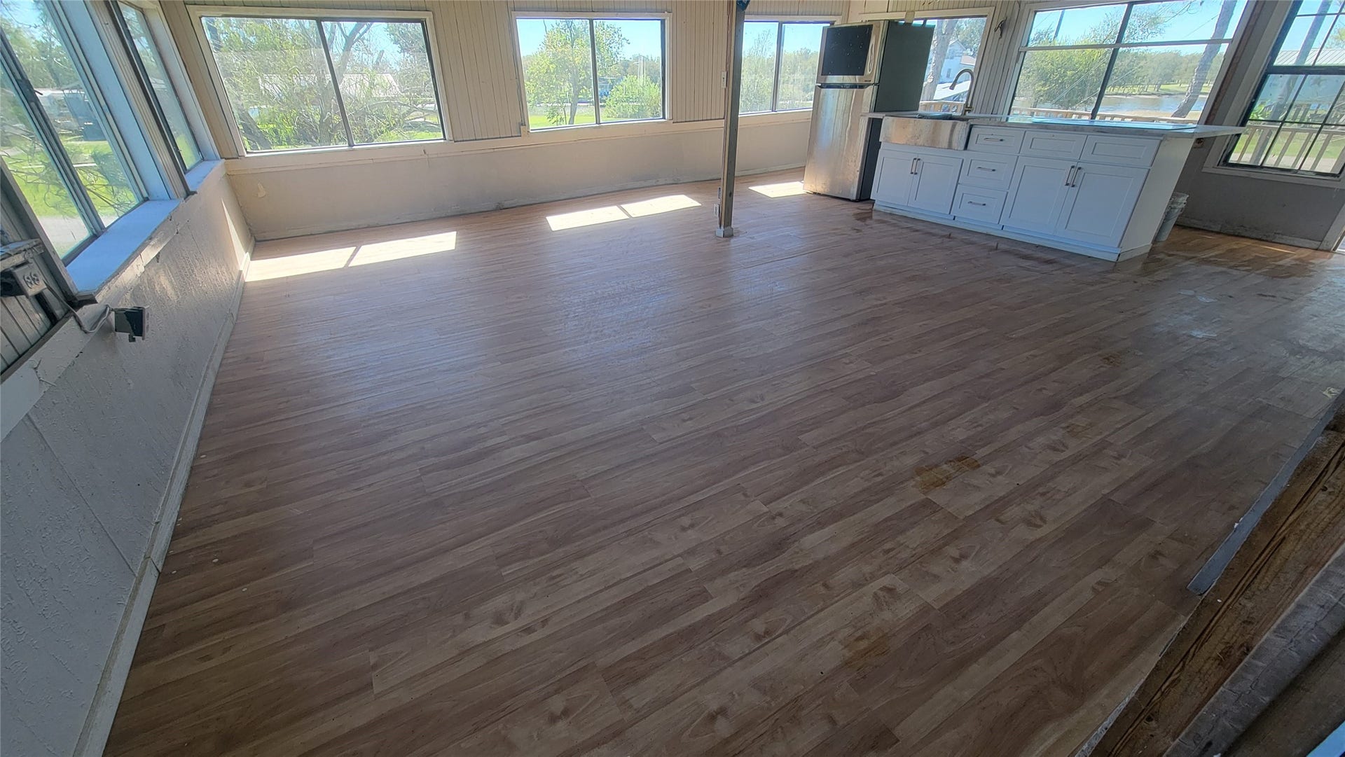 12018 Sandpiper Road, Angleton, TX 77515 This bright, open-concept room features expansive windows, wood flooring, and a modern kitchen area with a white island and cabinets. Perfect for enjoying natural light and views.