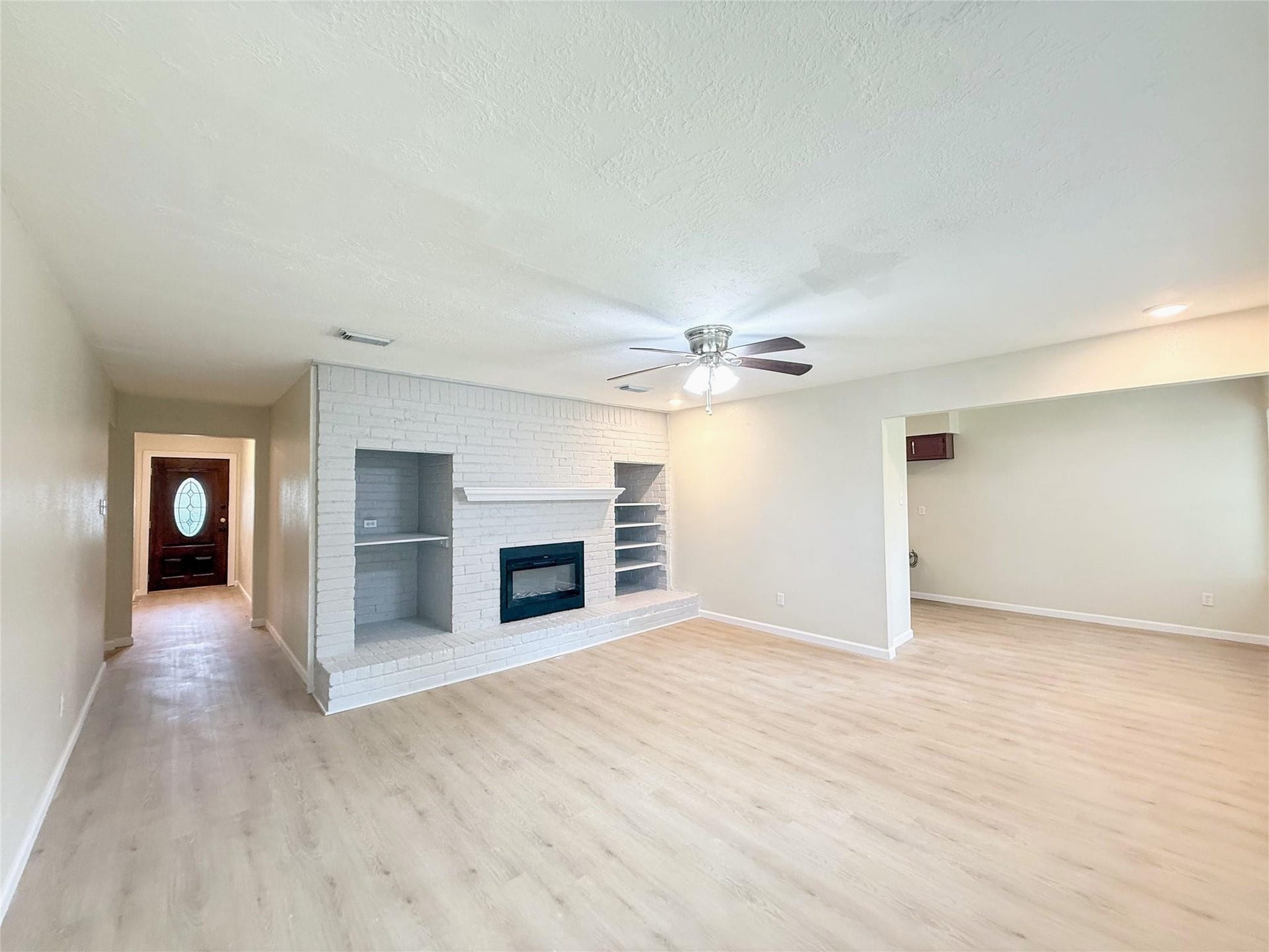 4251 Rosegate Drive, Spring, TX 77373 Bright, open living room featuring a white painted brick fireplace wall with a raised hearth and built-in shelving on both sides. Light wood flooring with an open flow into the adjoining dining area.