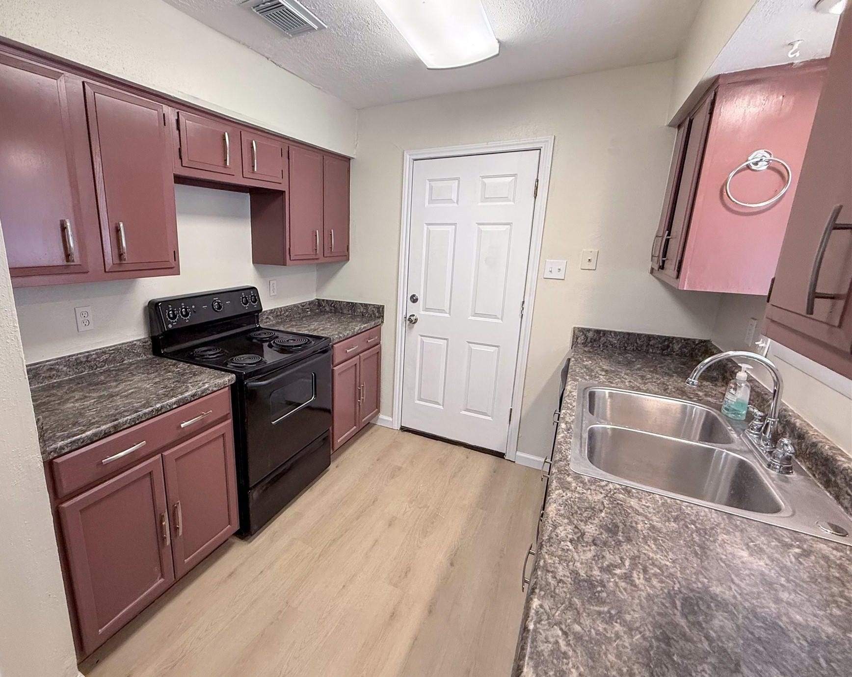 4251 Rosegate Drive, Spring, TX 77373 Galley kitchen with wood tone cabinets, dark countertops, a double stainless sink under the window, and wood flooring.