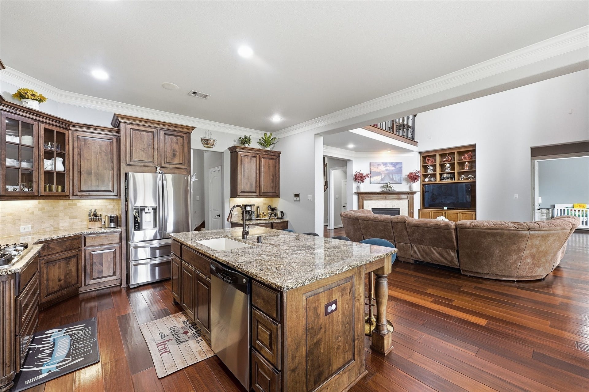 8311 Caroline Ridge Drive, Humble, TX 77396 Elegant open-concept kitchen and living area featuring rich wood cabinetry, granite countertops, and stainless steel appliances, seamlessly flowing into a cozy family room with a fireplace and built-in shelving.