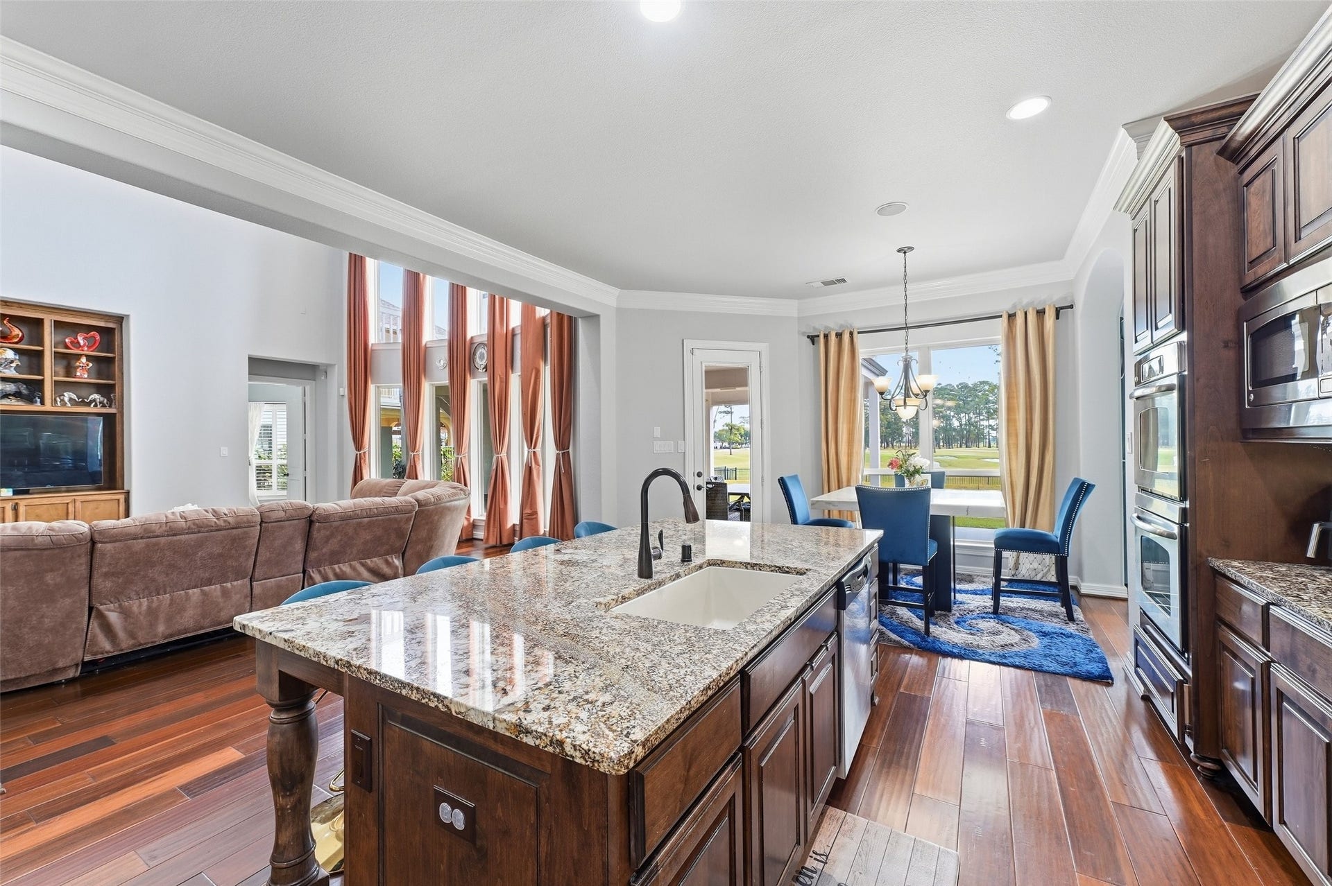 8311 Caroline Ridge Drive, Humble, TX 77396 Spacious open-concept living area with elegant wood floors, a modern kitchen island with granite countertops, and a cozy dining nook featuring large windows with scenic views.