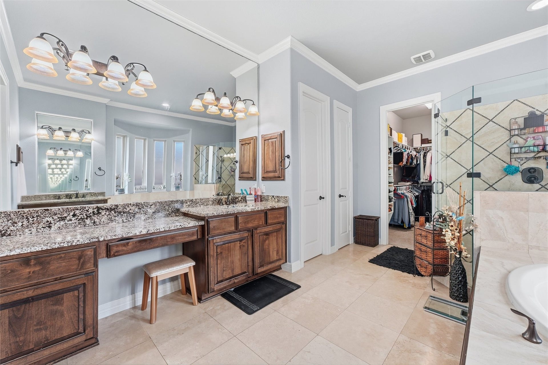 8311 Caroline Ridge Drive, Humble, TX 77396 Luxurious bathroom featuring a spacious double vanity with granite countertops, elegant lighting, and rich wood cabinetry. The room includes a walk-in closet, glass-enclosed shower, and a relaxing bathtub, all set against a backdrop of sophisticated tile work.