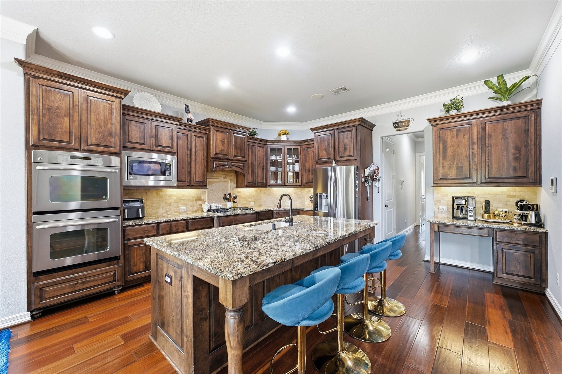 8311 Caroline Ridge Drive, Humble, TX 77396 A spacious kitchen featuring rich wooden cabinetry, a large granite island with seating, stainless steel appliances, and elegant wood flooring.